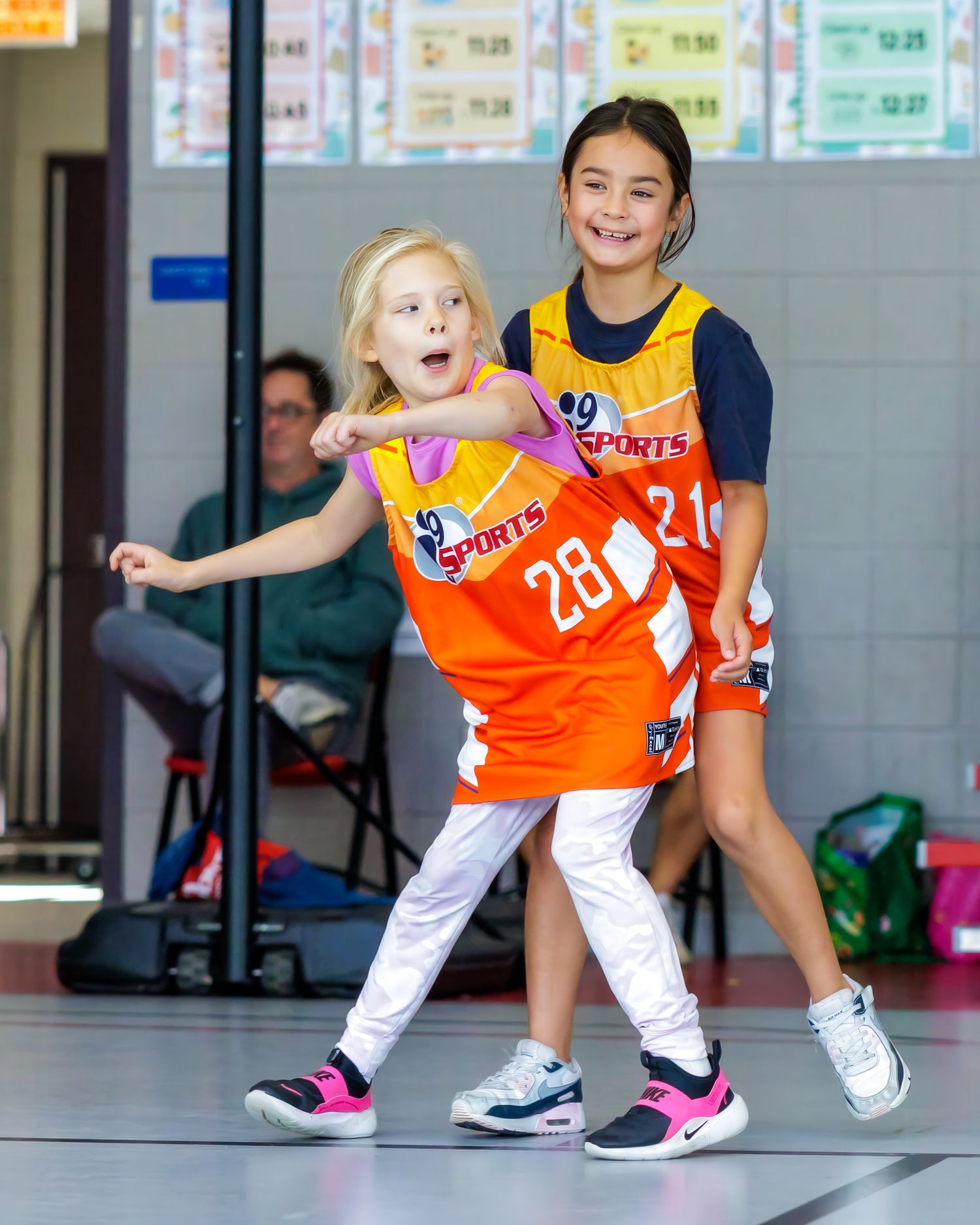 Young dancers in orange and white uniforms practice dance moves in a studio with mirrored walls.