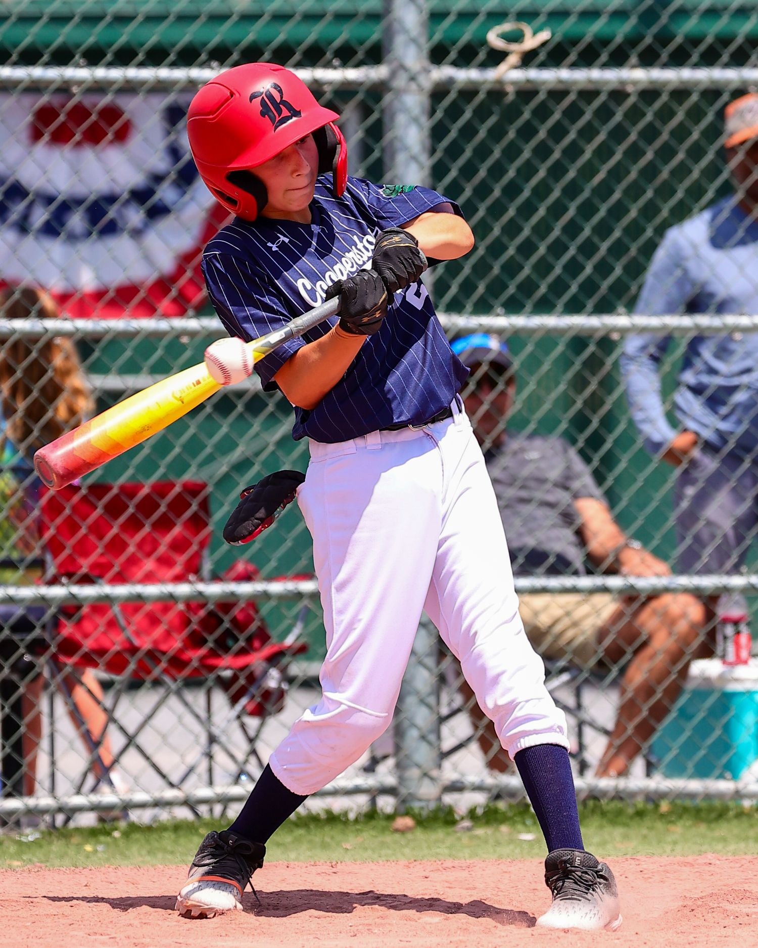 Baseball player in navy and white uniform swings bat during game with green fence visible in background.