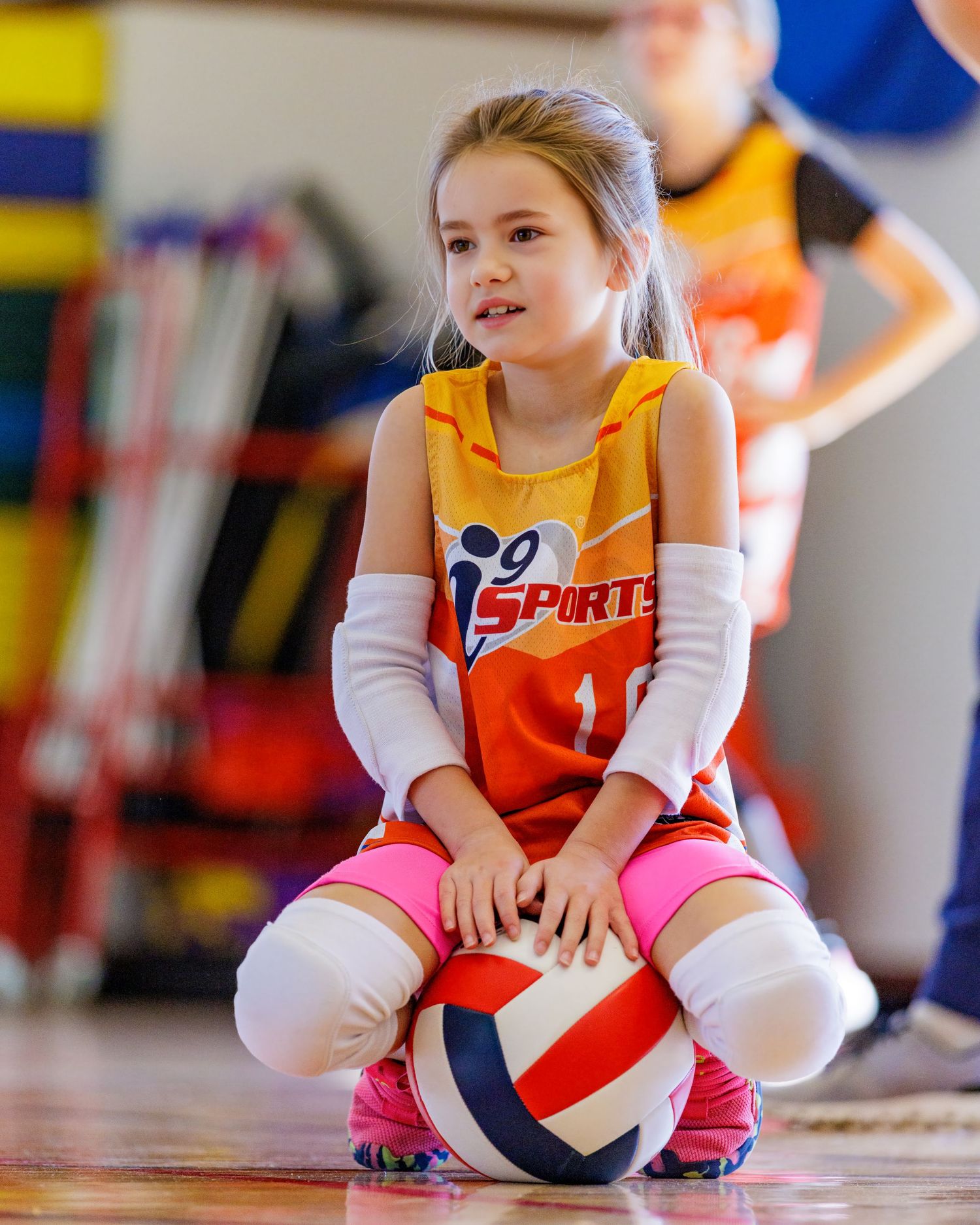 Young athletes in sports uniforms practice with a volleyball in a gym setting.