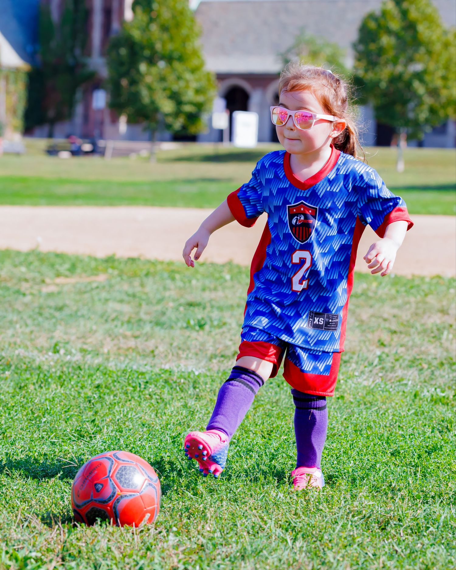 Children playing soccer on grass field wearing blue and red jerseys during practice.