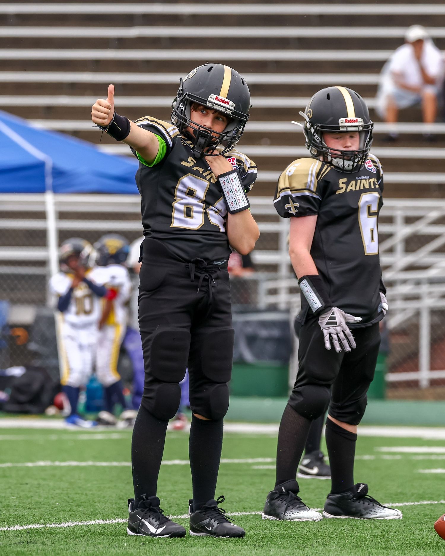 Two Saints players in black uniforms standing on field giving thumbs up.