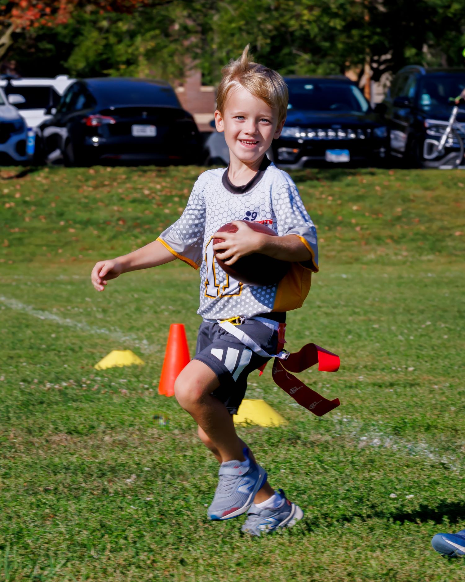 A young football player runs with determination across a grassy field during a flag football game.