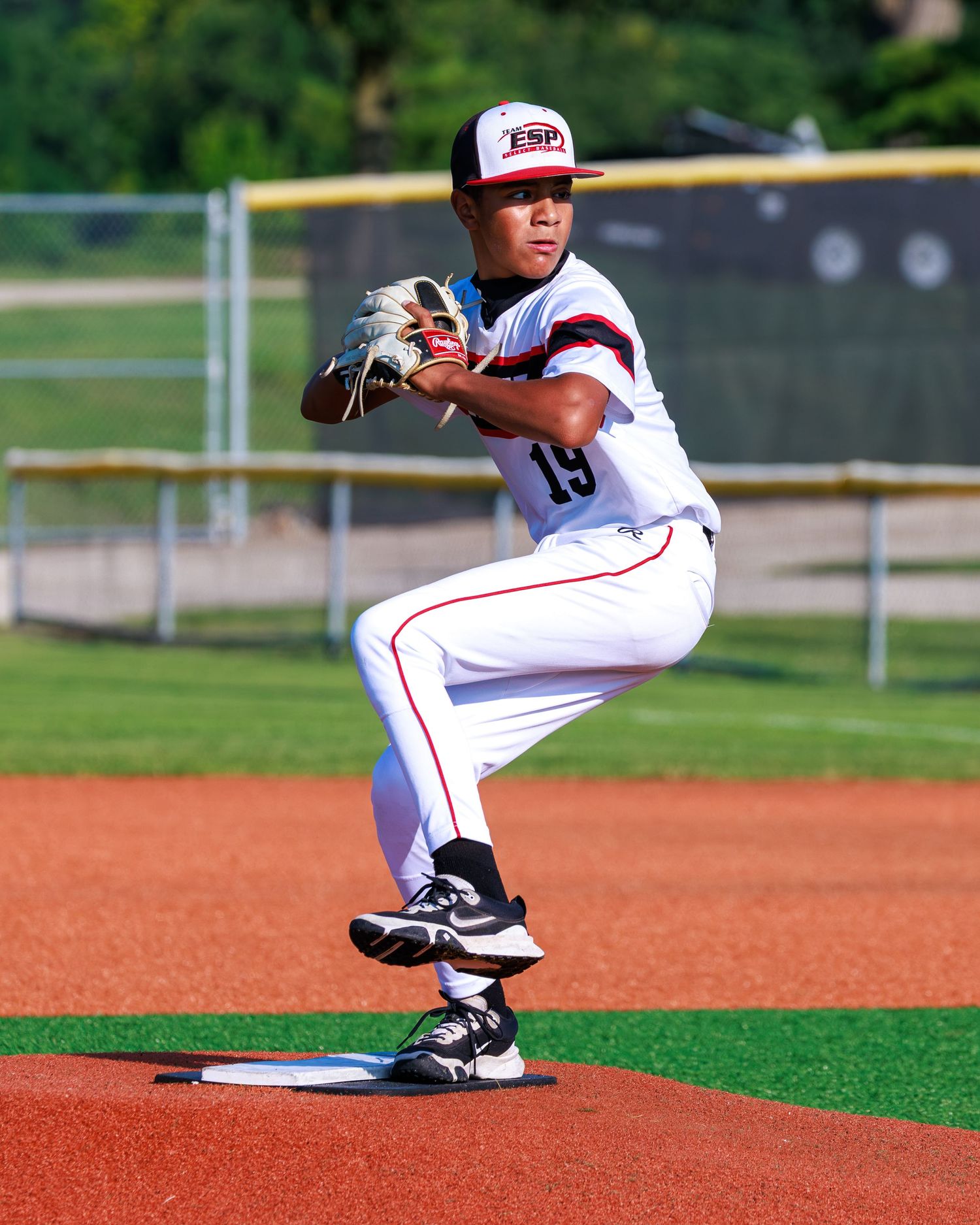 Young baseball pitcher in white uniform winds up on the mound during a youth league game on a sunny day.