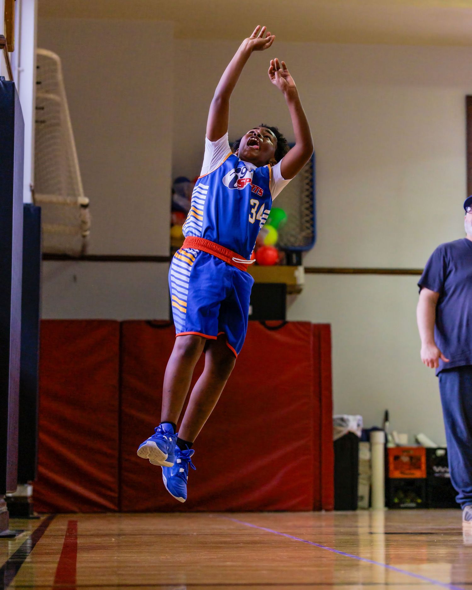 Basketball players in blue uniforms leap and jump during an indoor practice session.