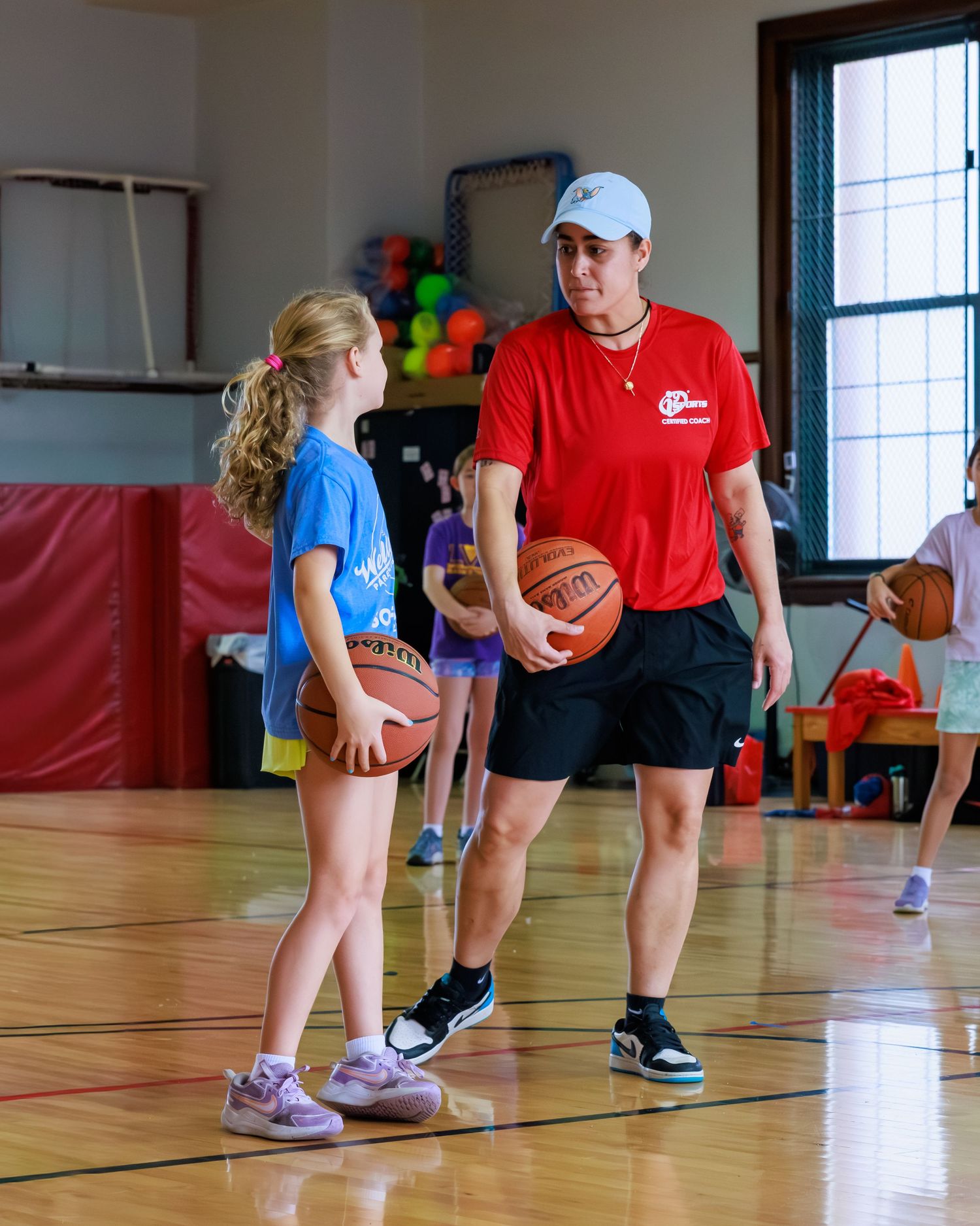 Basketball coach demonstrates dribbling technique to young players in a gymnasium during practice session.