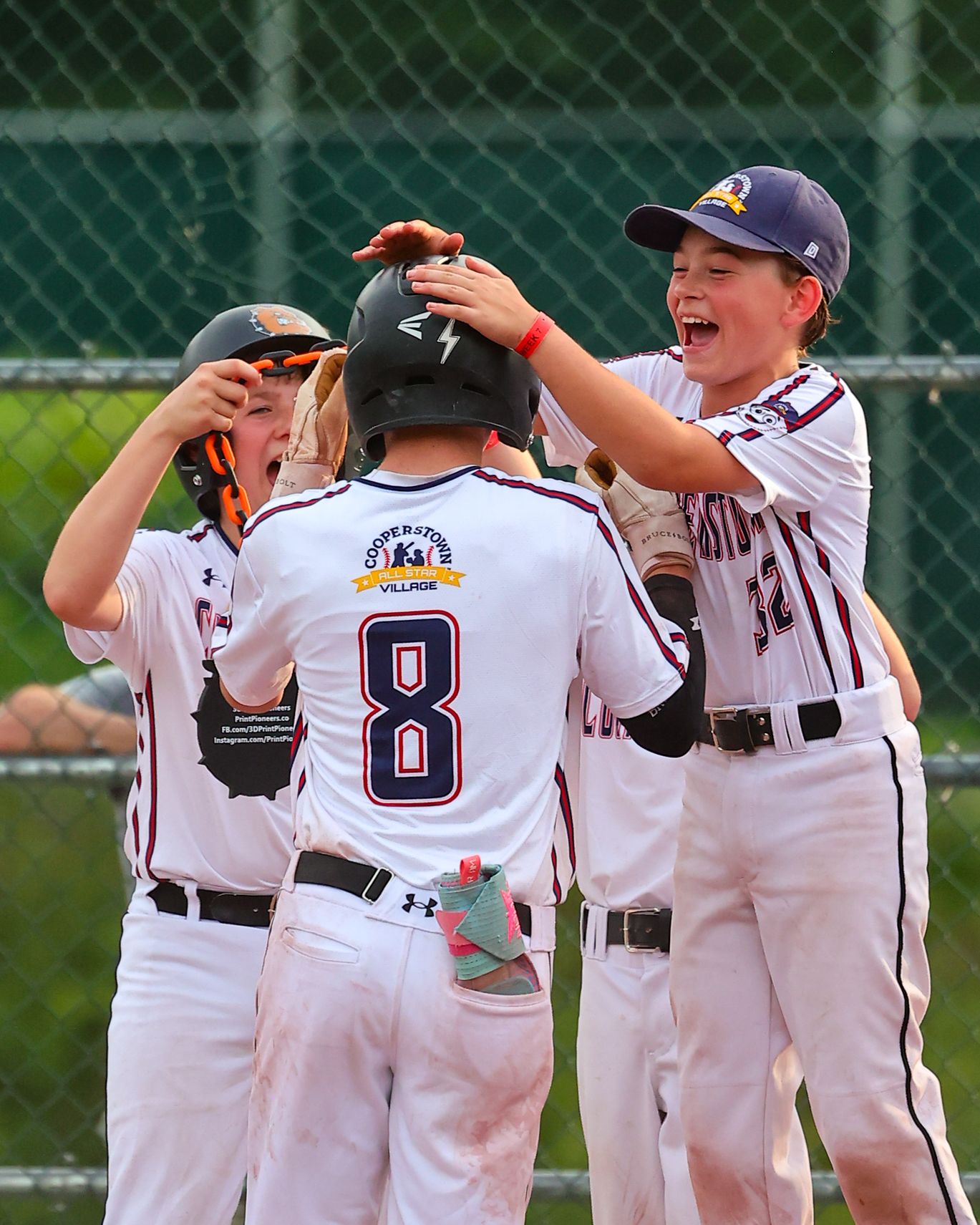 Youth baseball players celebrate with teammates in white uniforms after a homerun on the field.