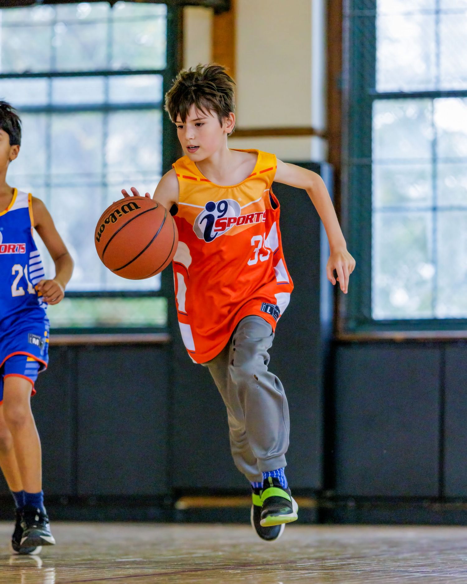 Kids in sports uniforms practicing basketball moves and footwork drills in gymnasium.