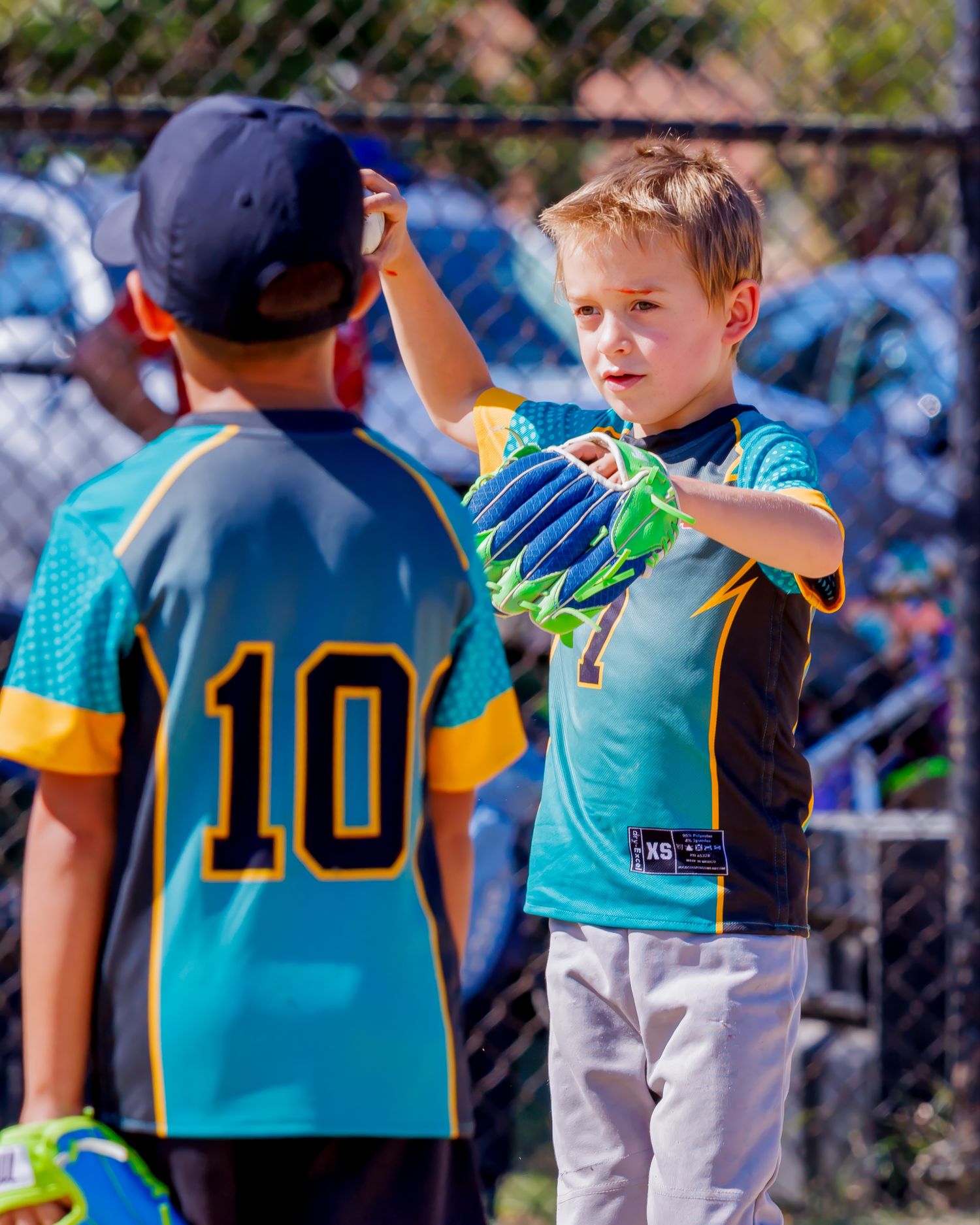 Youth baseball players in teal and yellow jerseys gather on a sunny field during a game.
