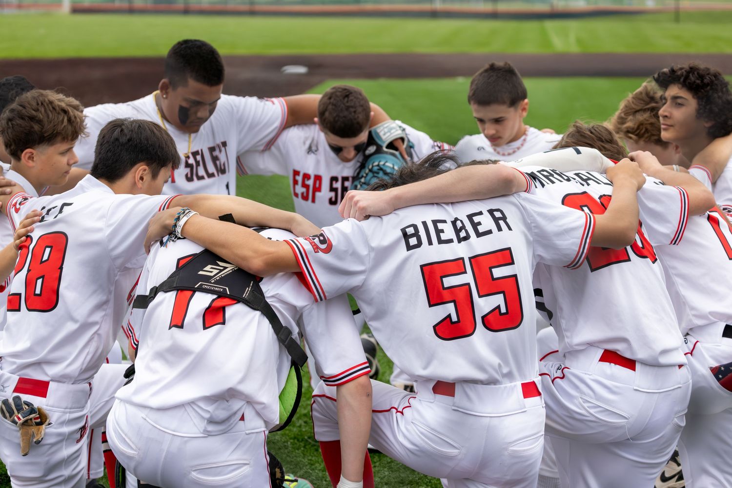 Baseball team players form a line with arms around shoulders showing unity and camaraderie on the field.