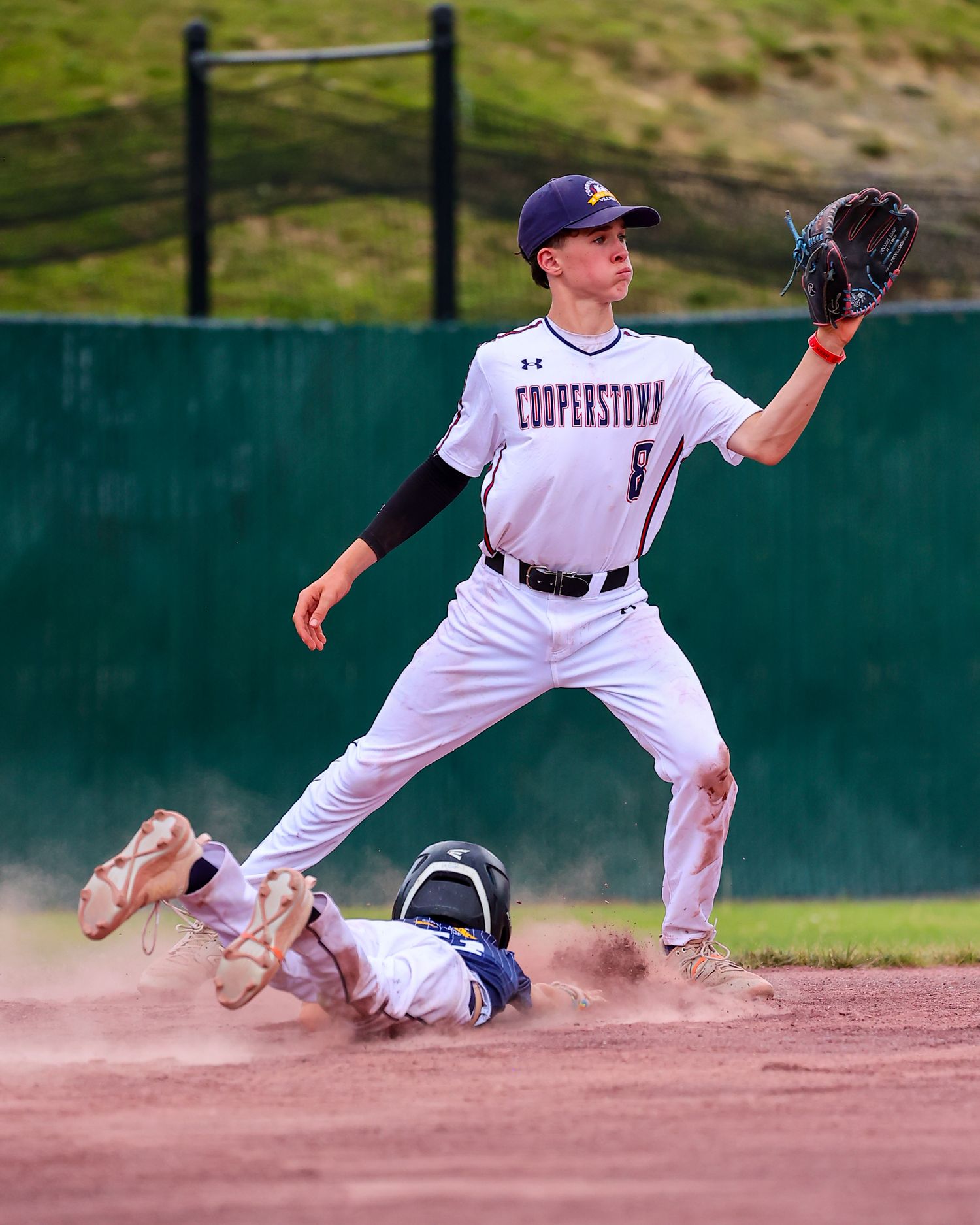 Baseball player sliding into base during intense game action with dust cloud visible around the play.