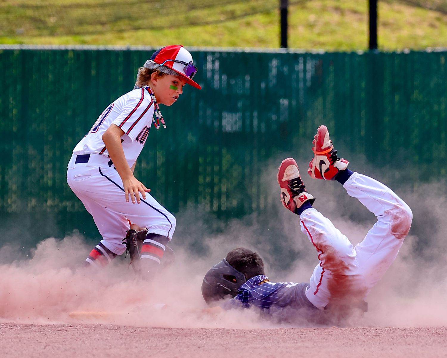 Baseball player slides into home plate creating a cloud of dust during an intense play at the plate.