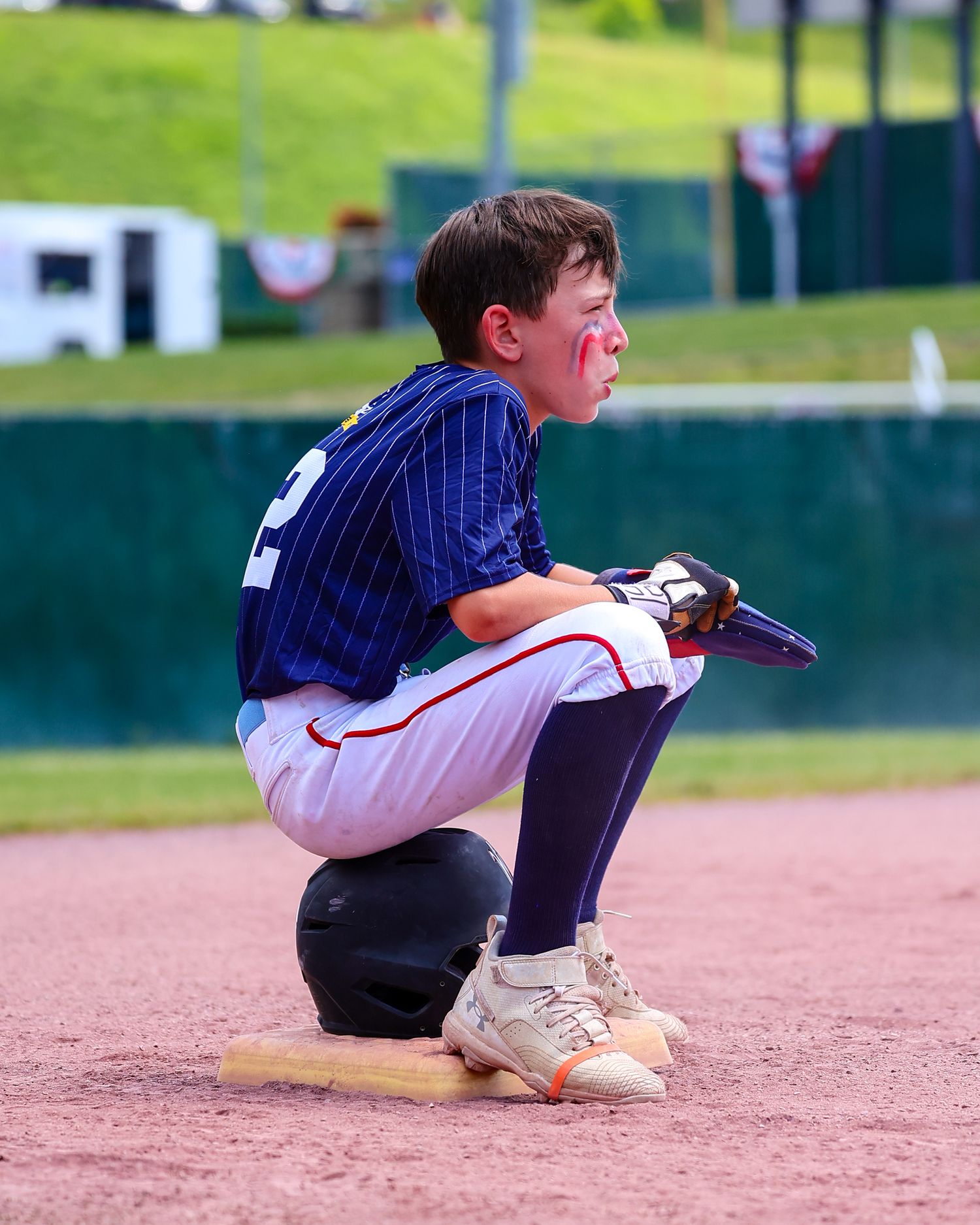 A baseball player slides into base during a youth league game on a sunny day.