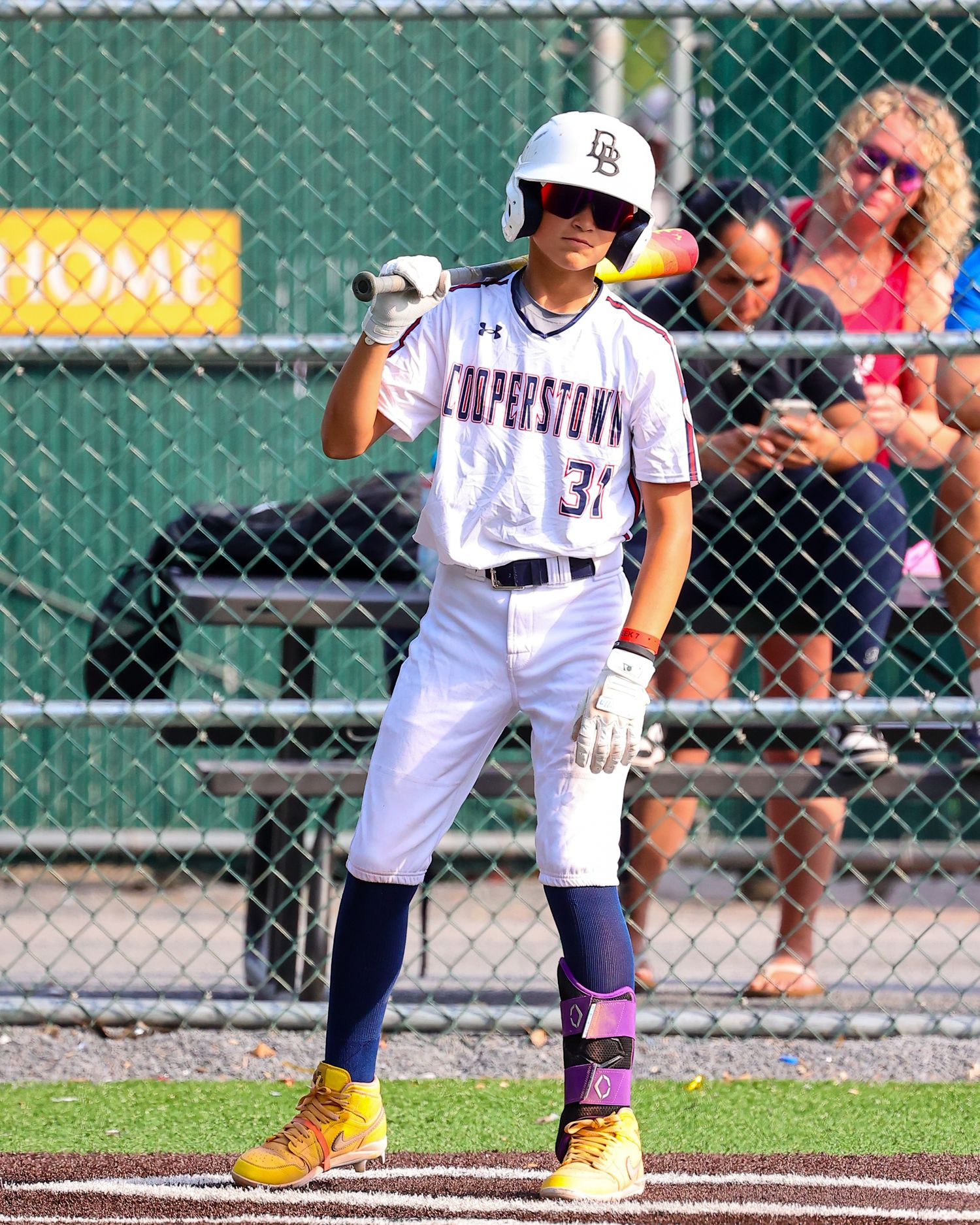 Baseball player in white uniform and yellow boots stands ready at home plate during a game.