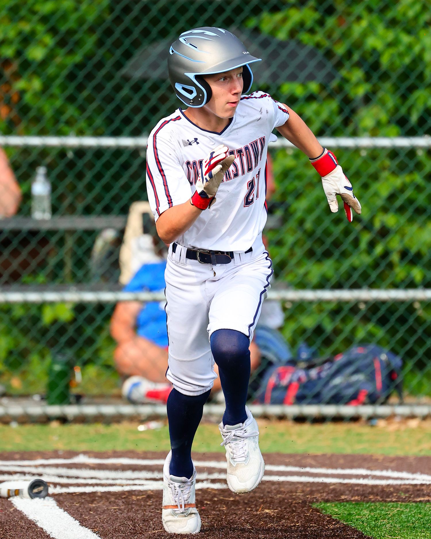 Baseball player in white running towards first base during game with dirt kicking up around cleats.