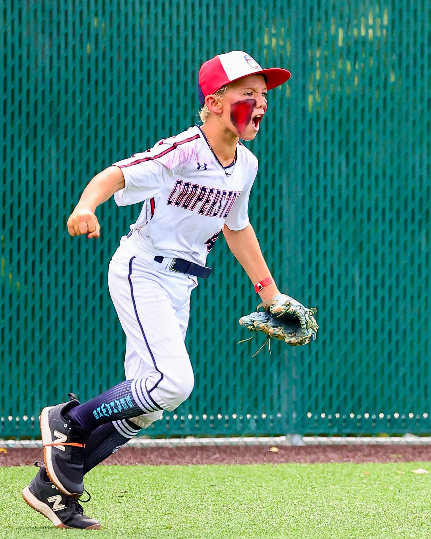 Baseball player in white uniform celebrates passionately on the field during a game with green wall background.