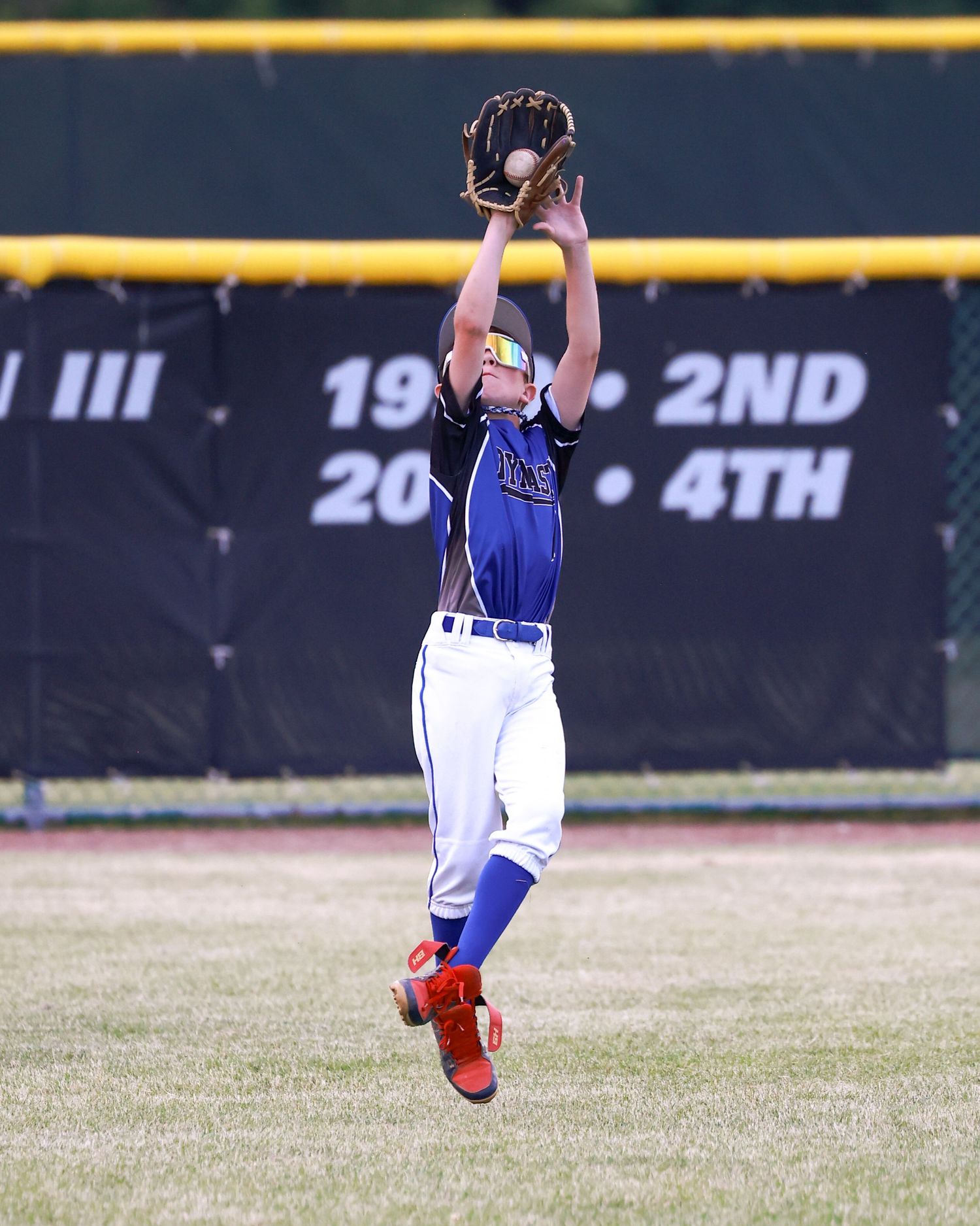 Baseball outfielder diving horizontally to catch a fly ball in a blue and white uniform.