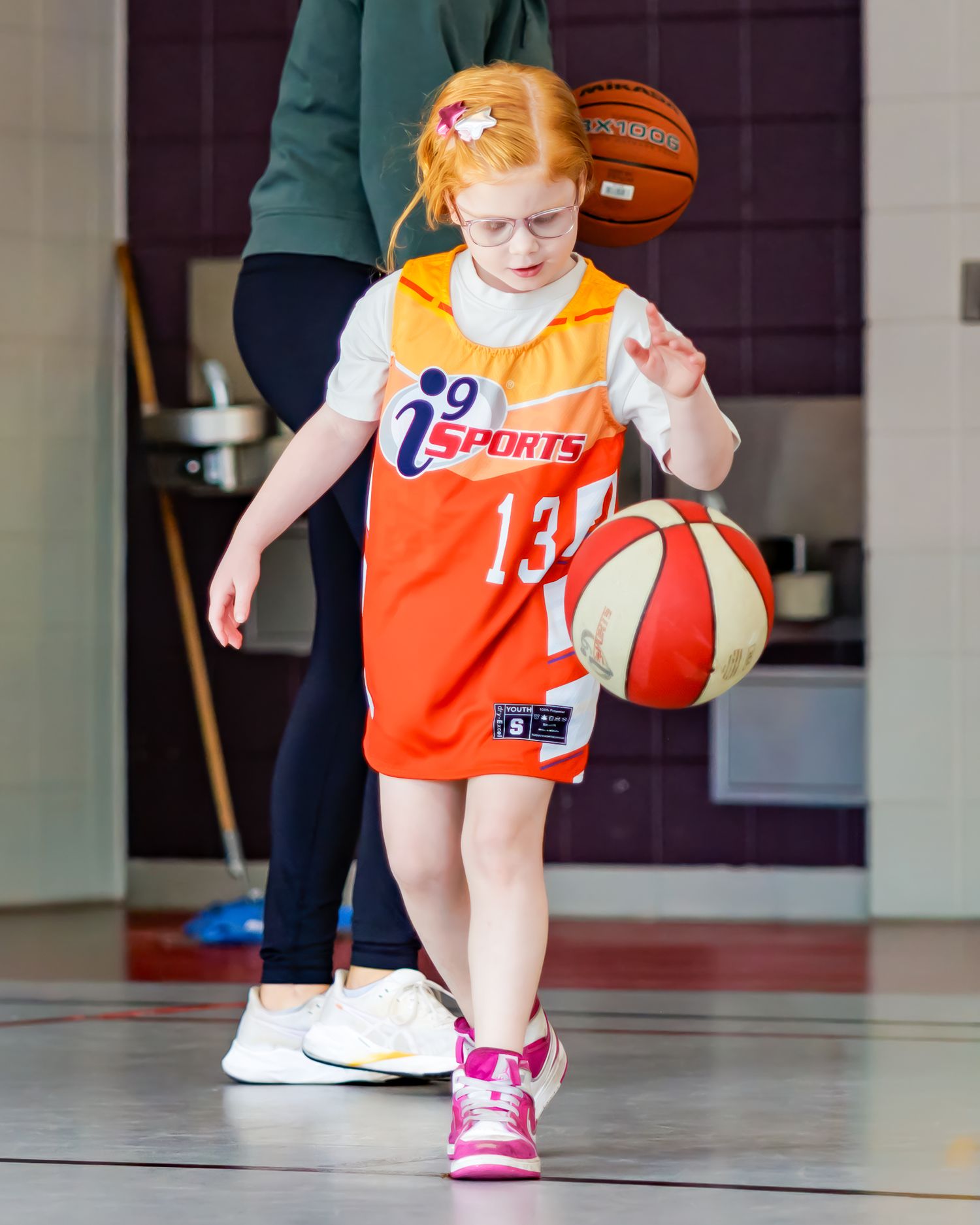 Young basketball player in orange jersey dribbles ball during practice in indoor gym.