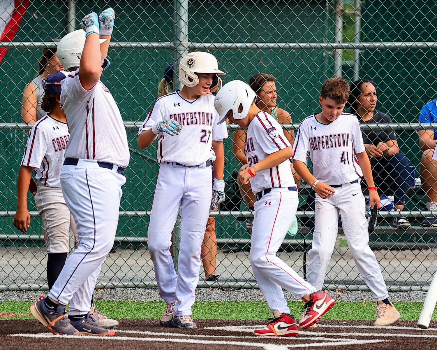 Baseball players in white uniforms celebrate at home plate after scoring during a game.