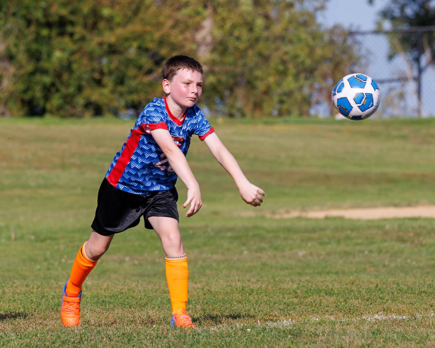 Soccer player in orange socks and blue jersey kicking ball on sunny grass field during daytime match.