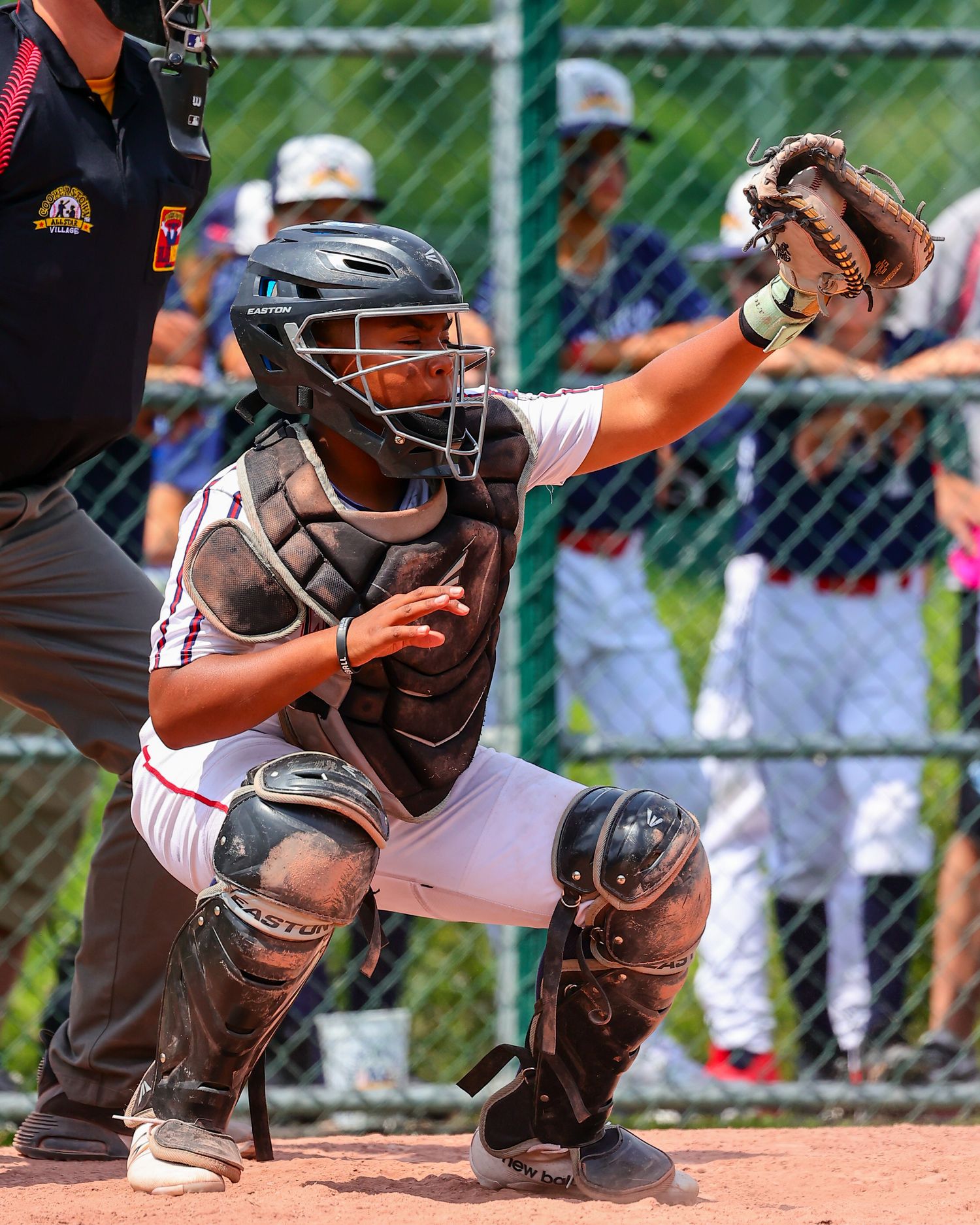 Baseball catcher in protective gear crouches in ready position behind home plate during game.