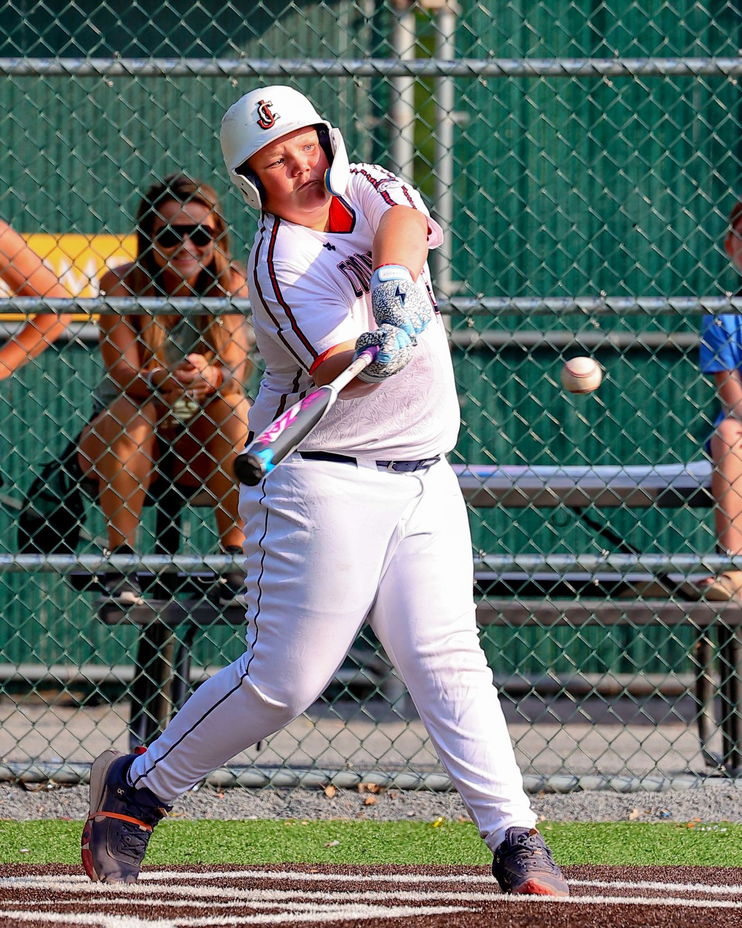 Baseball player in white uniform executes a perfect bunt during a game, with the ball making contact near home plate.