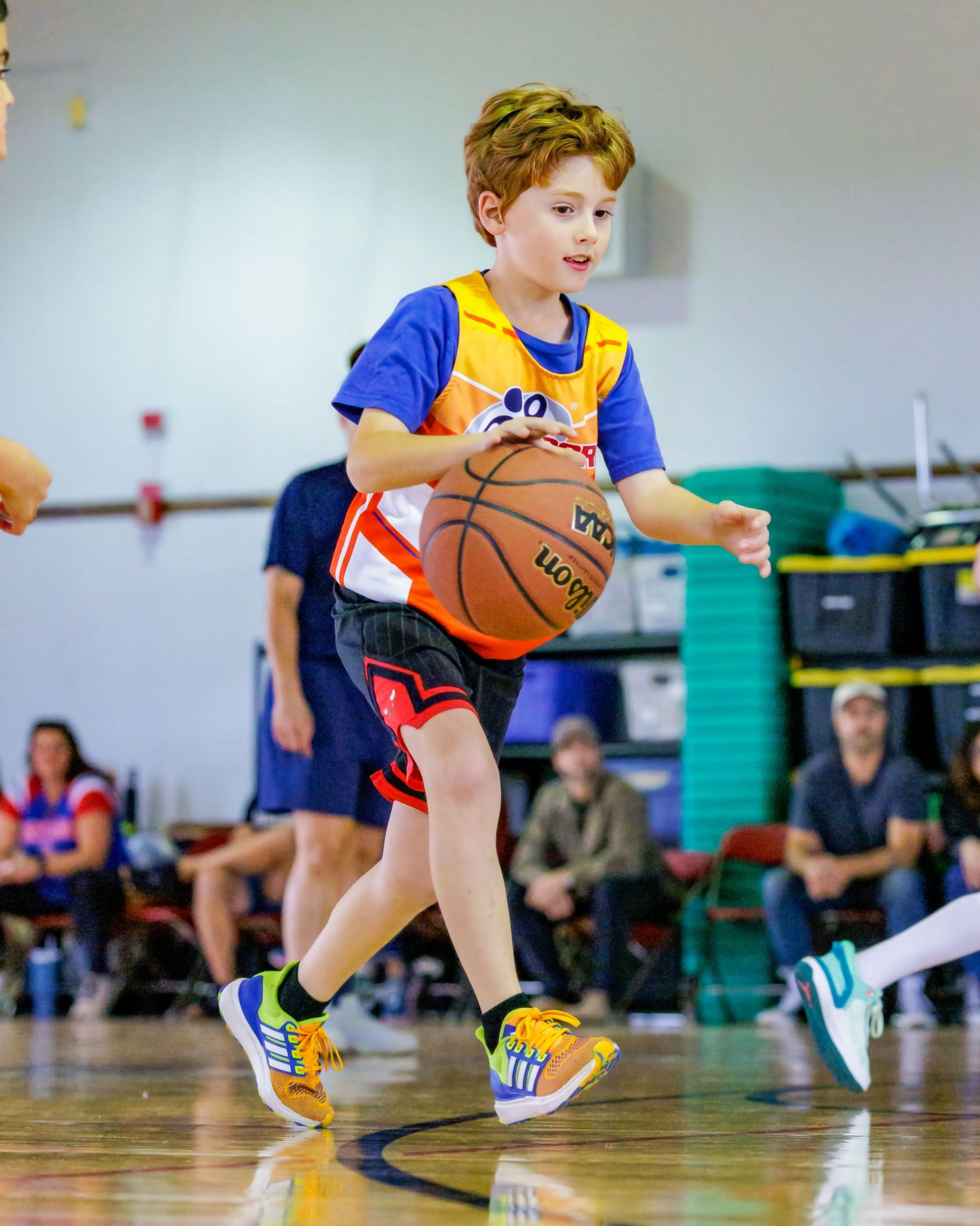 Young basketball player in blue and yellow uniform dribbles energetically across indoor court during youth game.