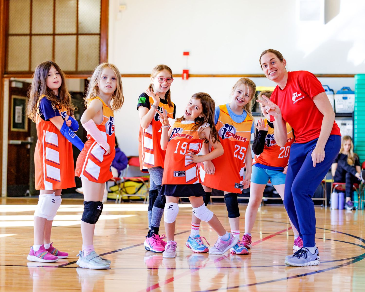Children in colorful sportswear participating in a group exercise or warmup session in a gymnasium.