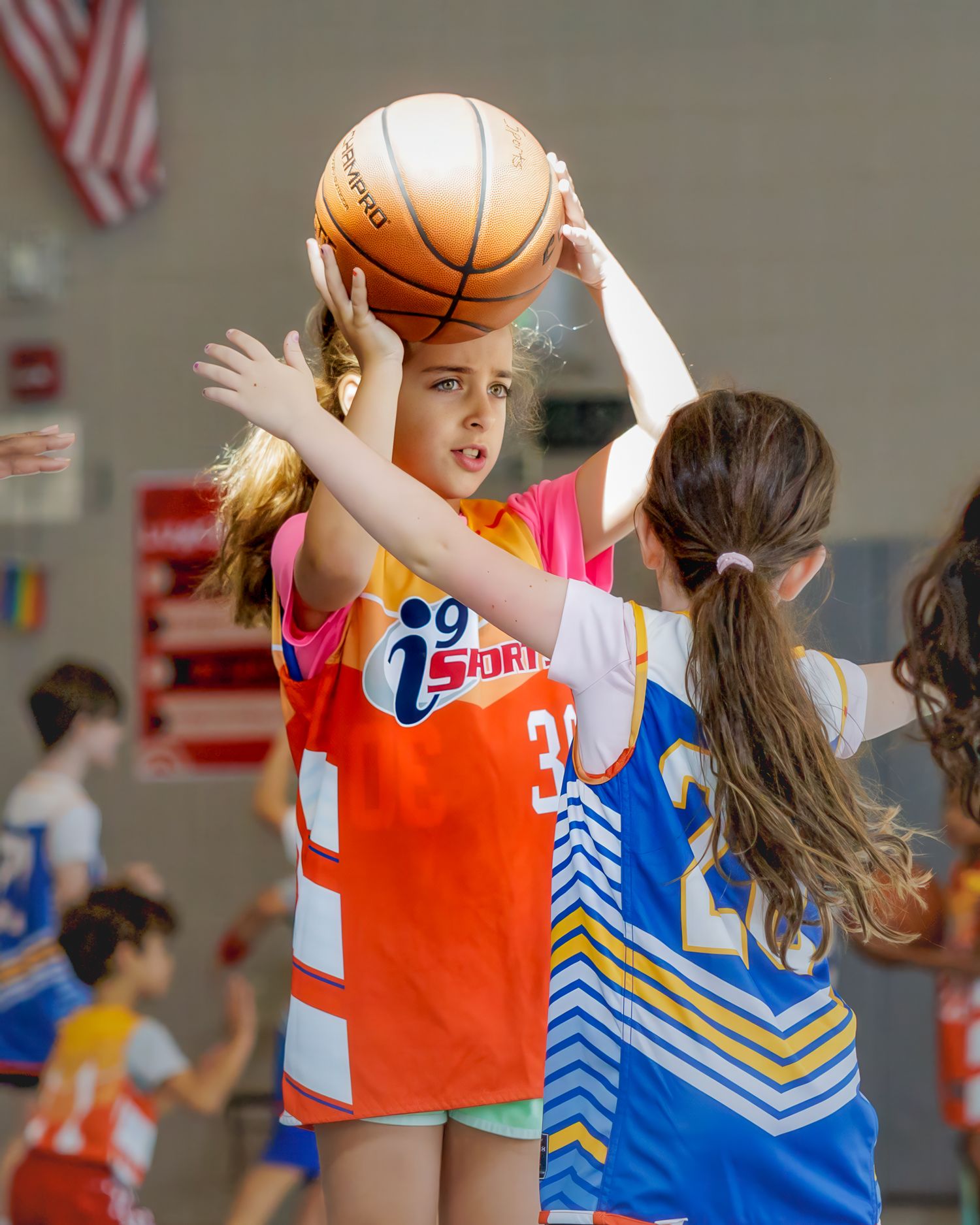 Two basketball players in orange and blue uniforms compete for possession during a game.