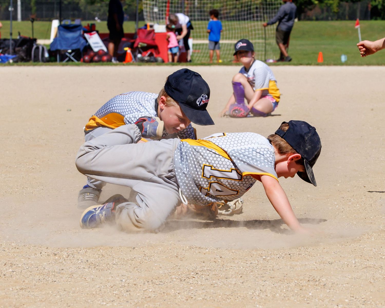 Baseball player slides into base during intense game action creating dust cloud on field.