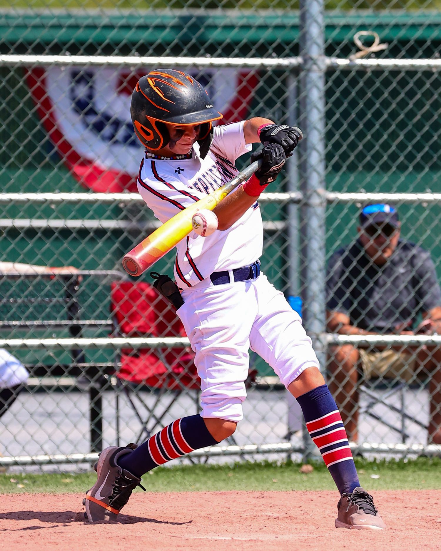Baseball batter in white uniform takes a powerful swing at bat during a youth game.