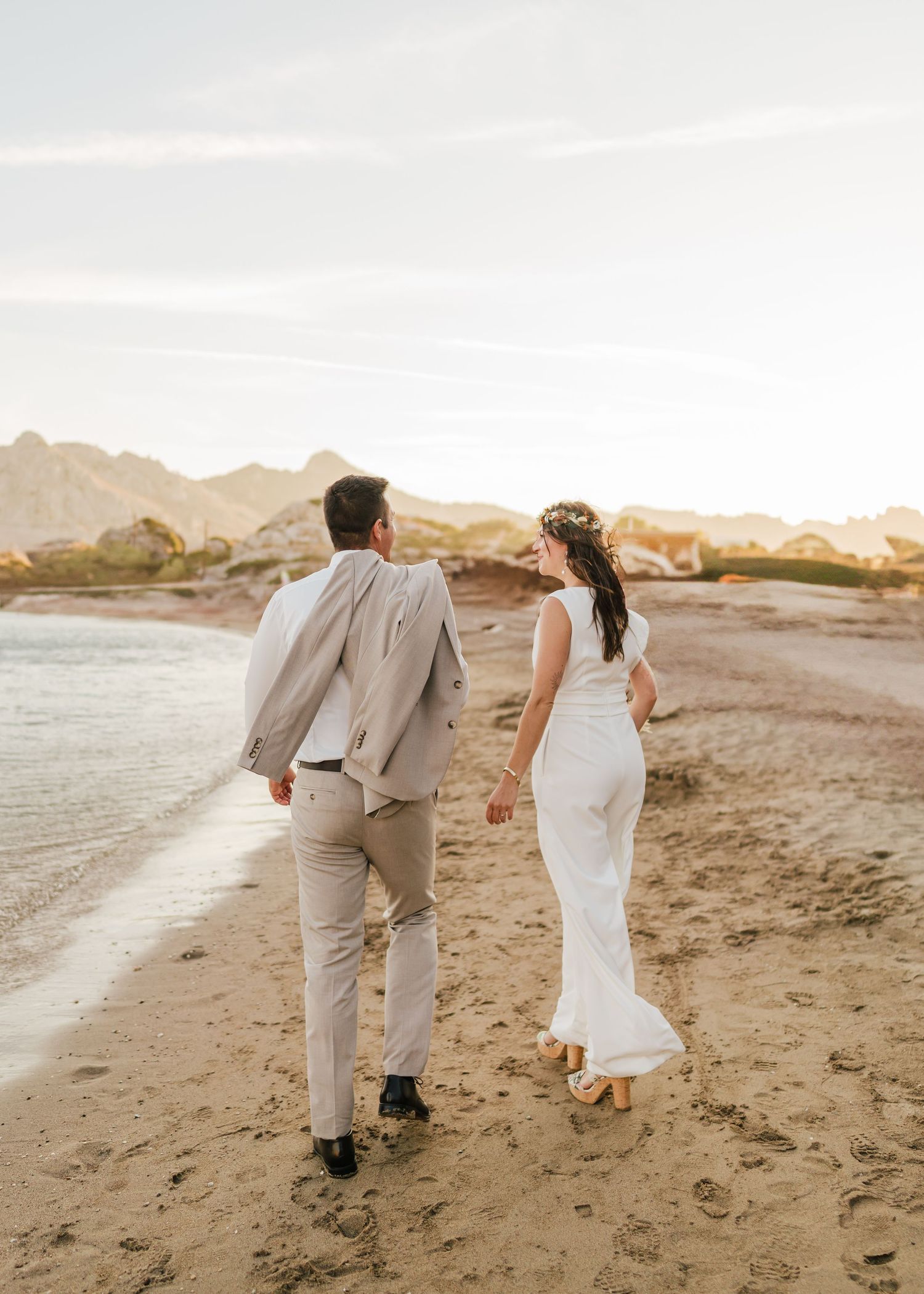 Ein Paar geht Hand in Hand an einem malerischen Strand mit Bergen im Hintergrund entlang. Hochzeiten Griechenland - Hochzeitsfotograf Rhodos