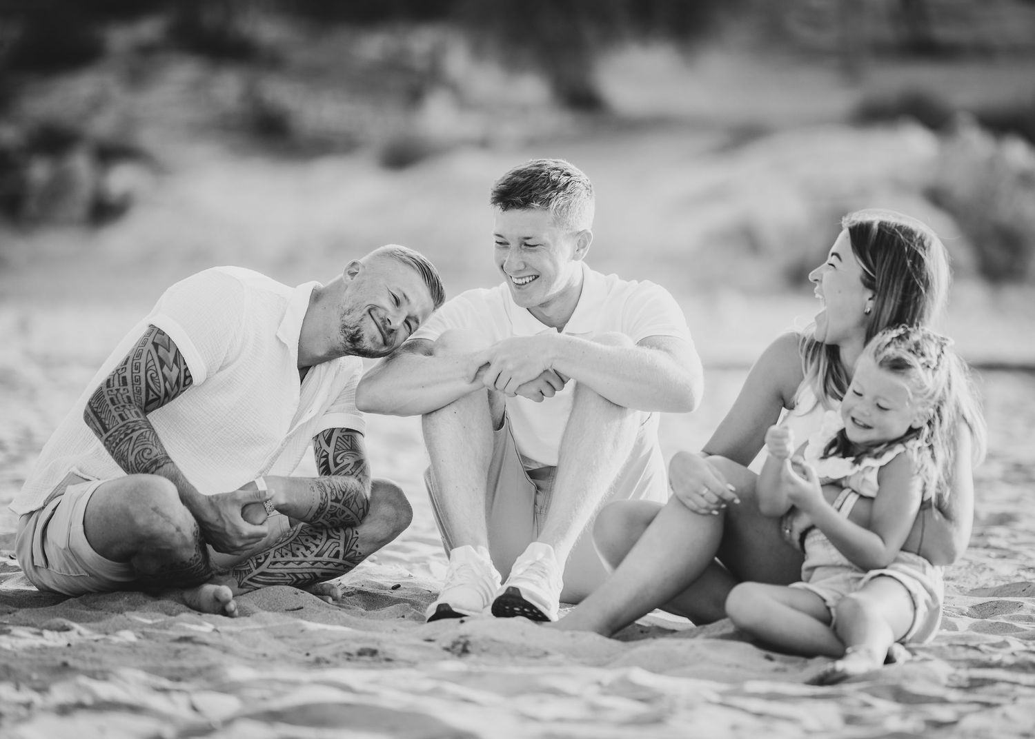 Black and white photos of a couple laying playfully on the beach sand. Fotograf Rhodos