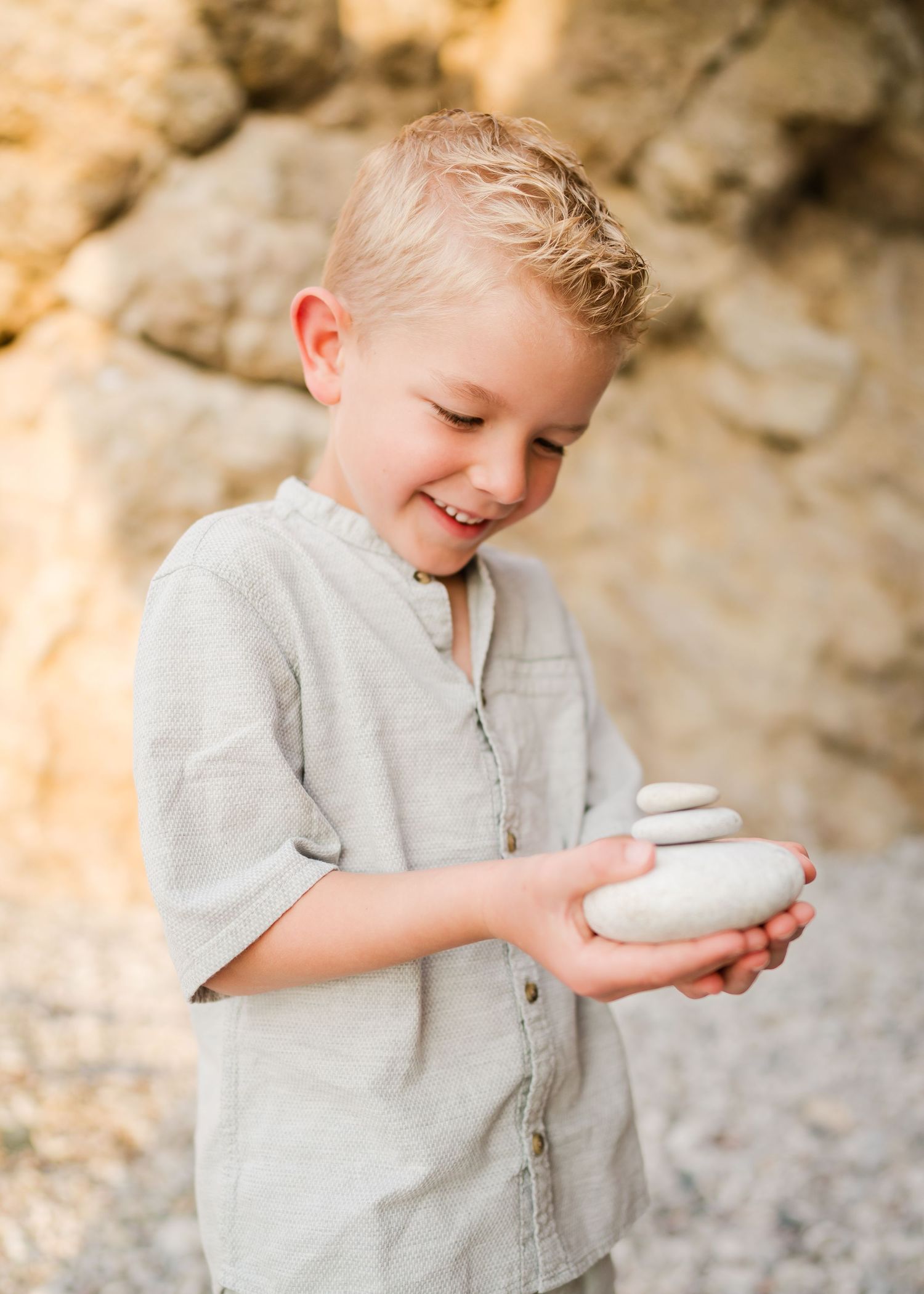 Child in gray shirt examining white stones on rocky beach with joyful expression. Fotograf Rhodos