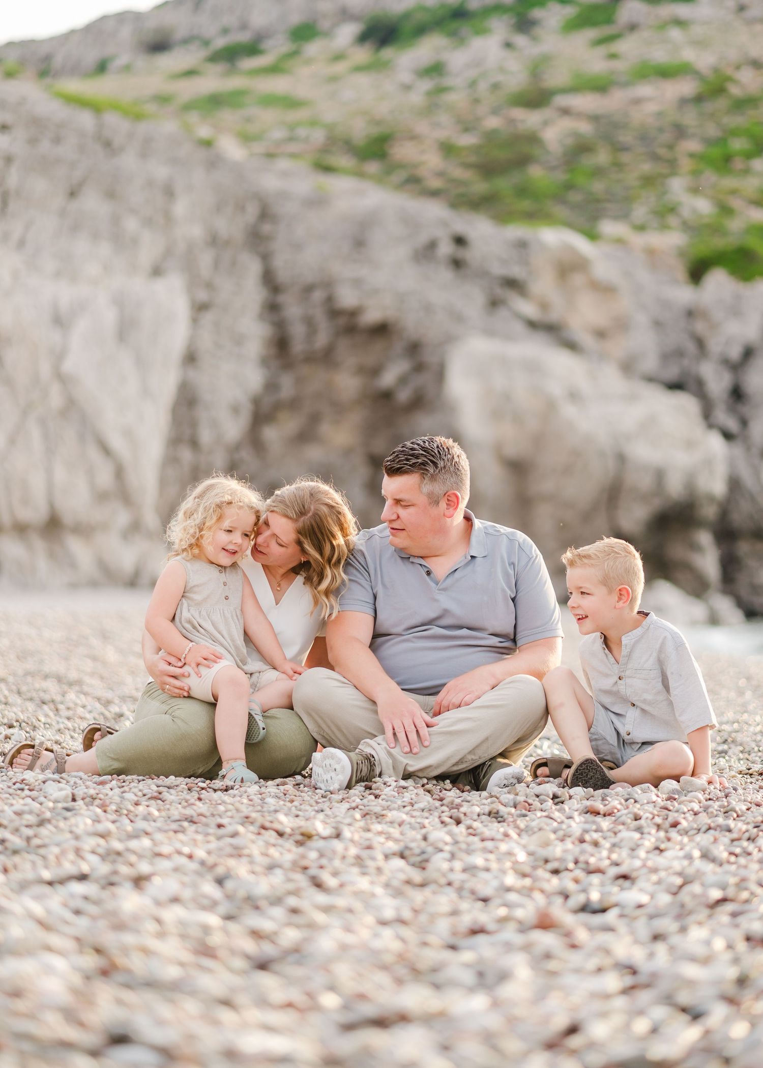 A family sits together on a pebble beach near rocky cliffs. Fotograf Rhodos