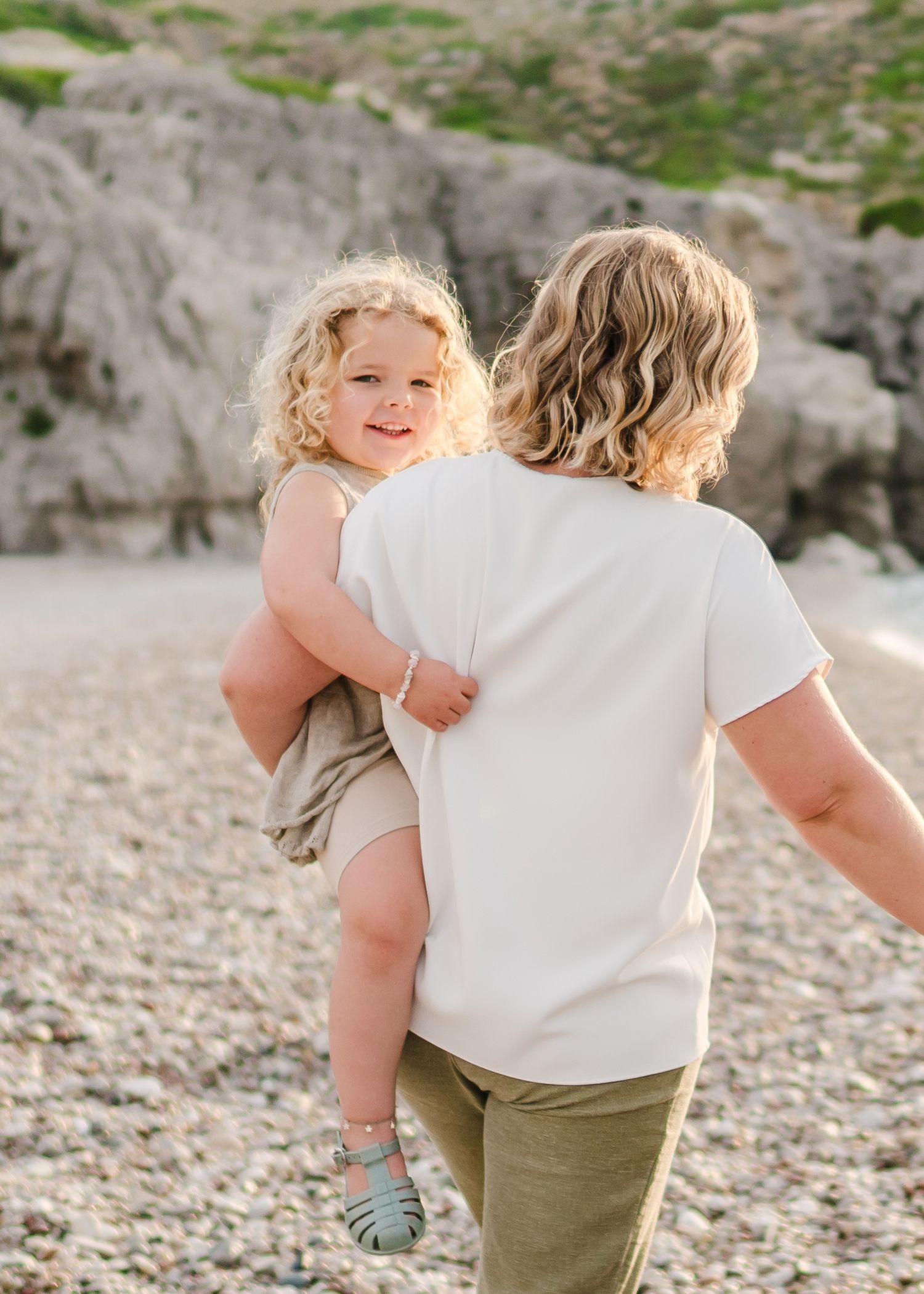Parent carrying child along rocky beach during sunset photography session. Fotograf Rhodos