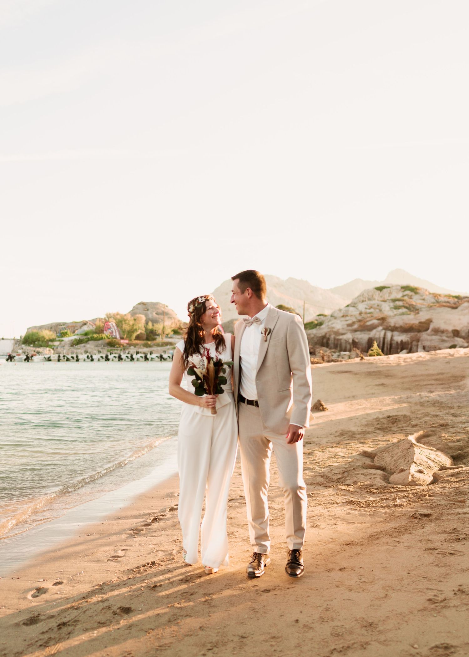 Paar in Hochzeitskleidung spaziert bei Sonnenuntergang an einem malerischen Strand entlang. heiraten am Strand - Hochzeitsfotograf Rhodos Ti