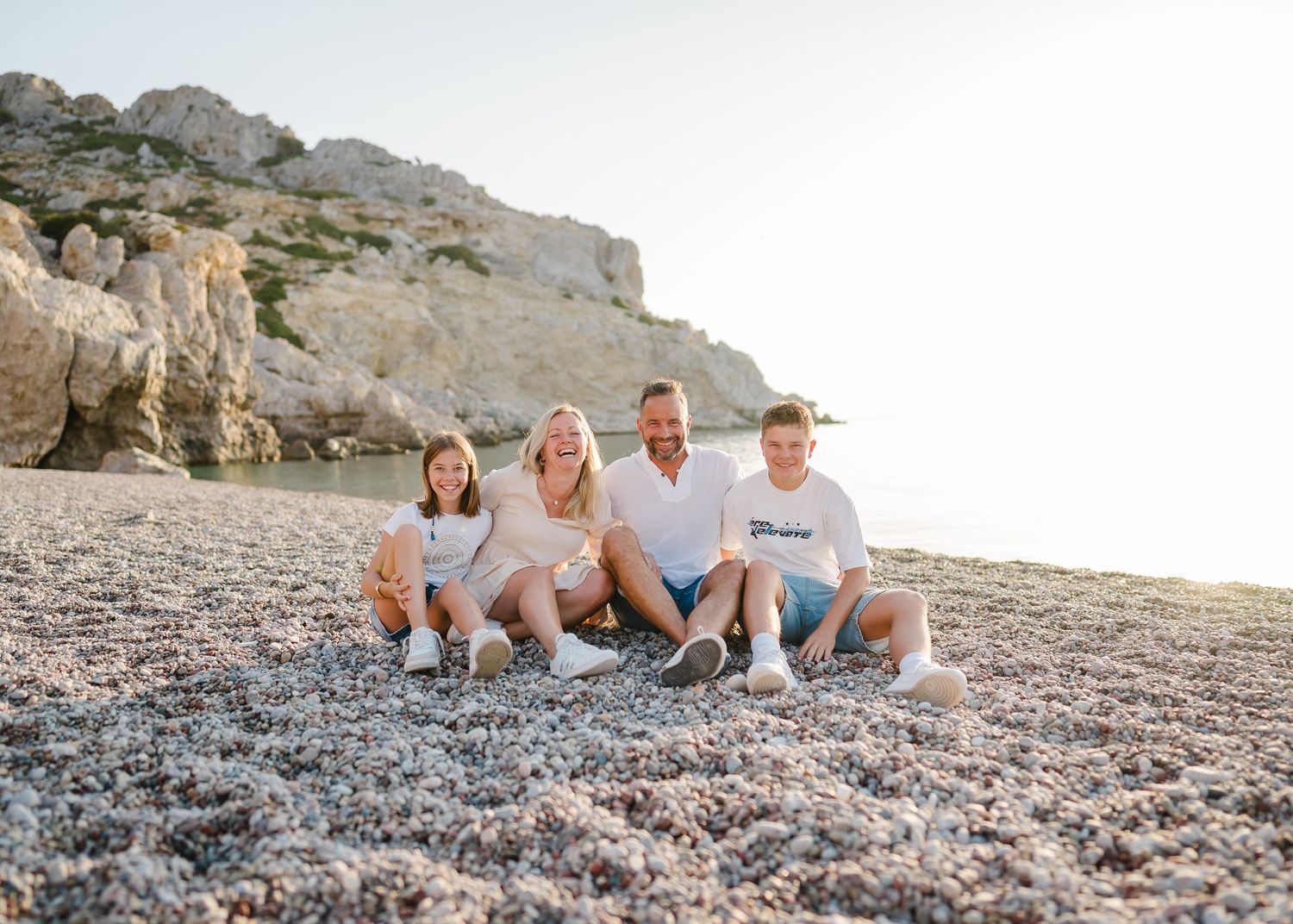 A group relaxing together on a rocky beach with cliffs in the background during golden hour. Fotograf Rhodos