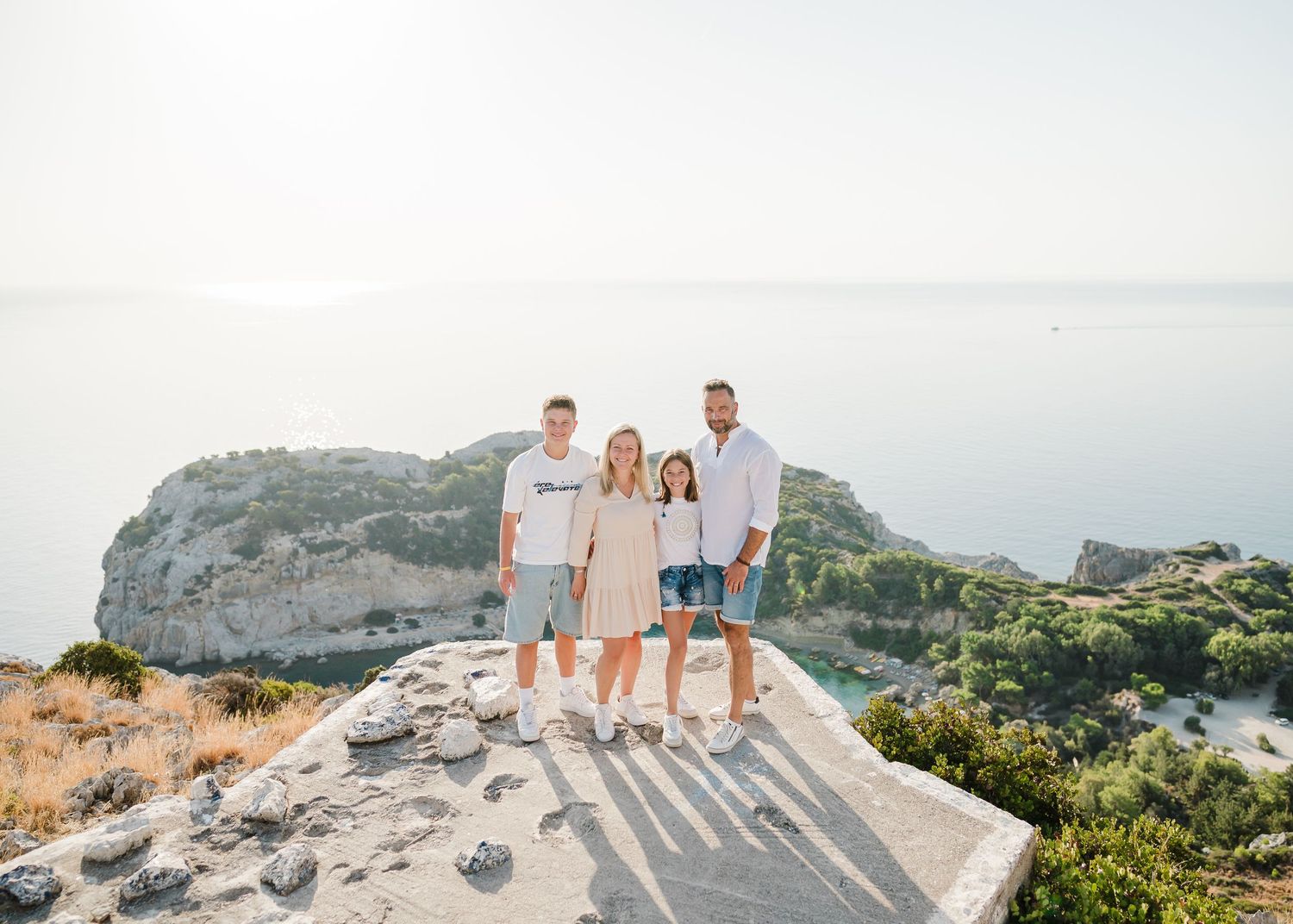 Family standing together on rocky overlook with scenic Mediterranean coastline in background. Fotograf Rhodos