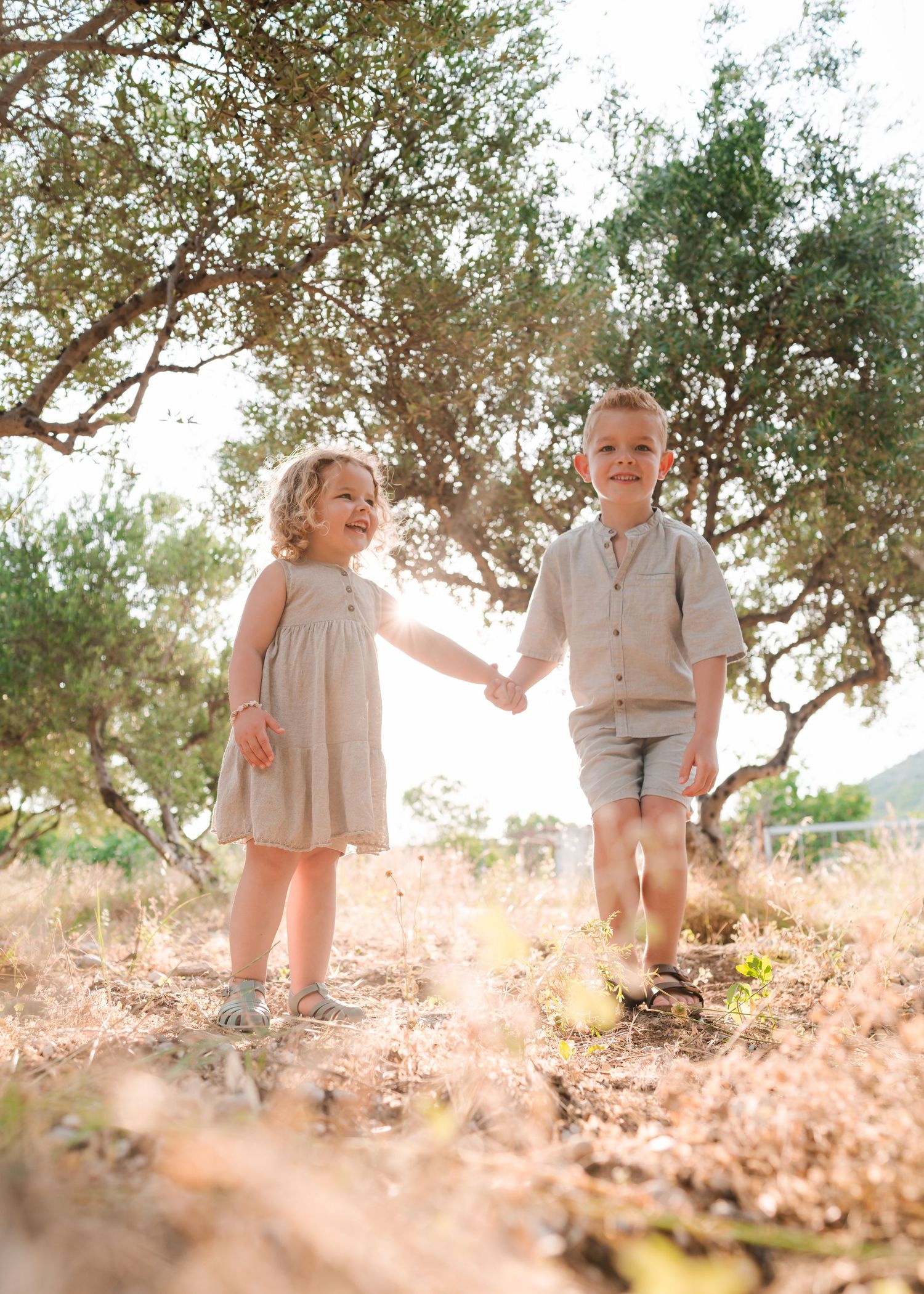 Two children walking and holding hands while exploring under trees in afternoon light. Fotograf Rhodos