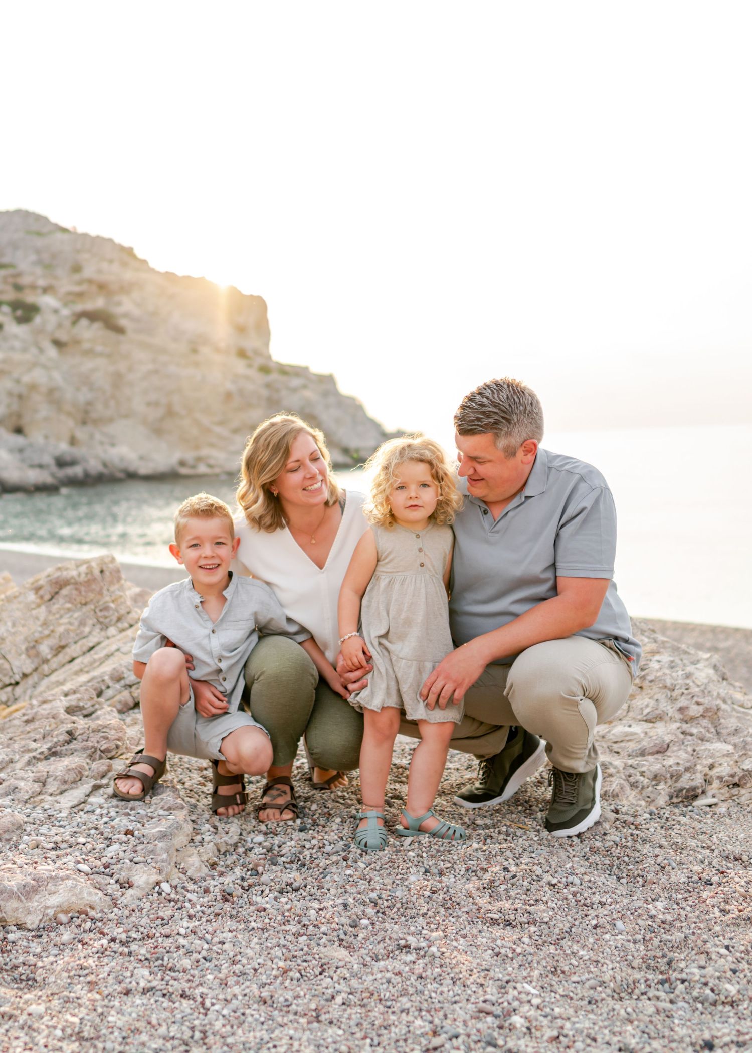 A family sits together on rocky coastal terrain during golden hour sunset at the beach. Fotograf Rhodos