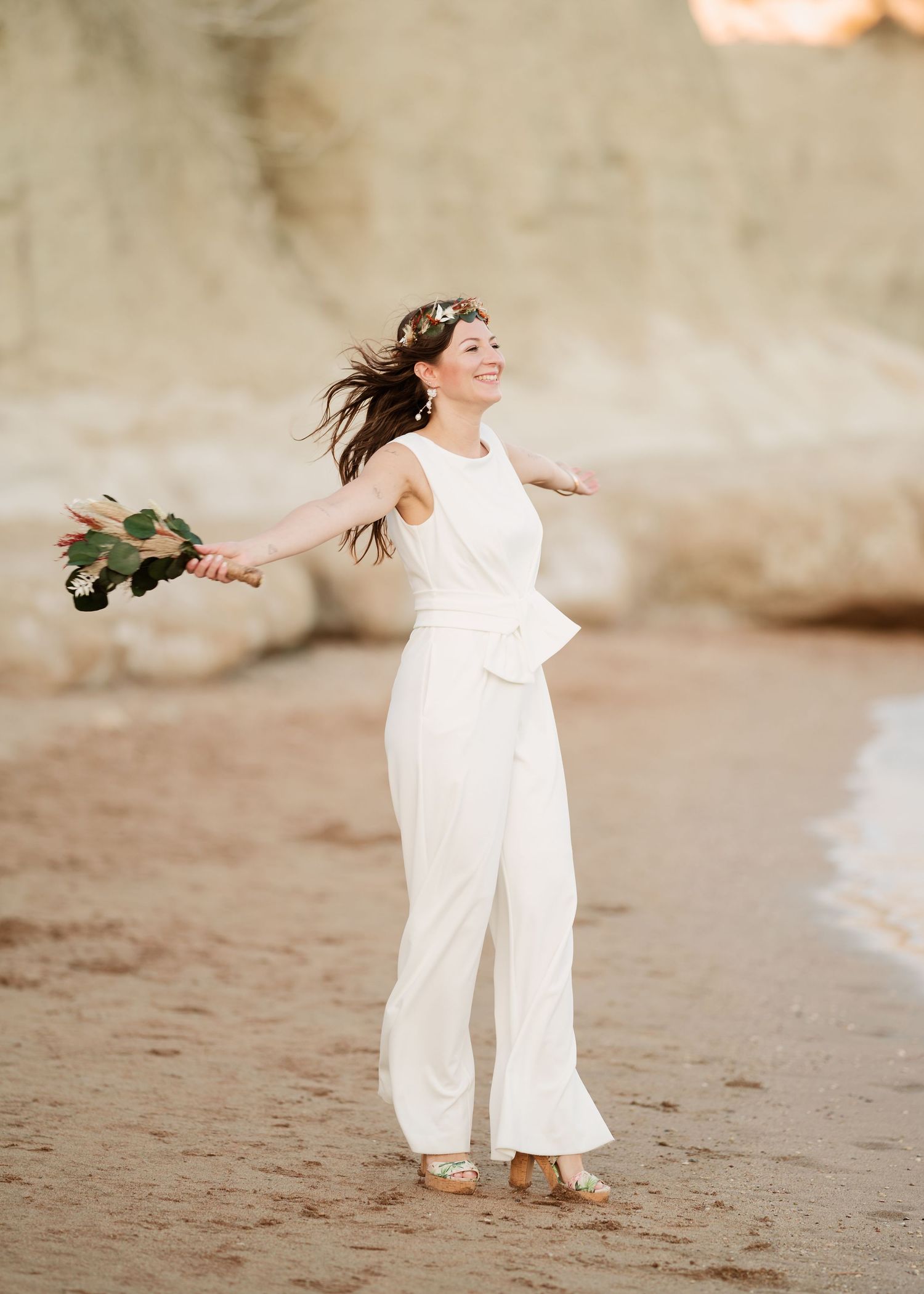 Braut im modernen weißen Overall, der mit ausgestreckten Armen am Sandstrand wirbelt. Hochzeiten Griechenland - Hochzeitsfotograf Rhodos Tin