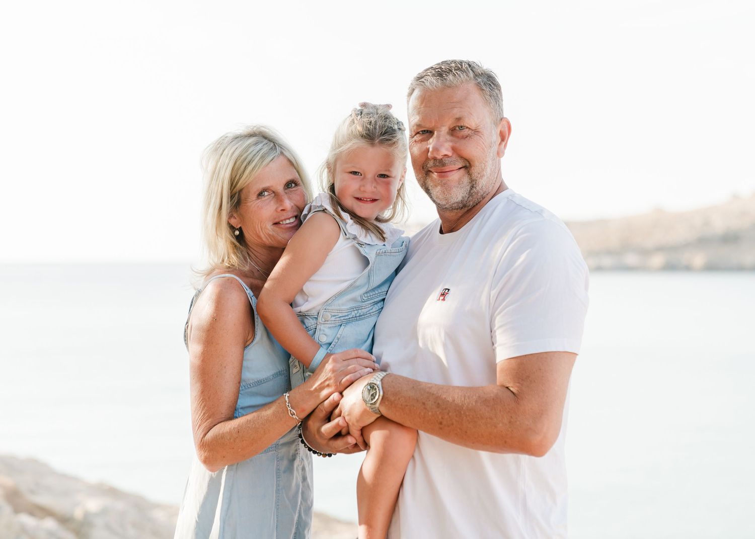 Family poses together at beach during golden hour with coastal cliffs in background.