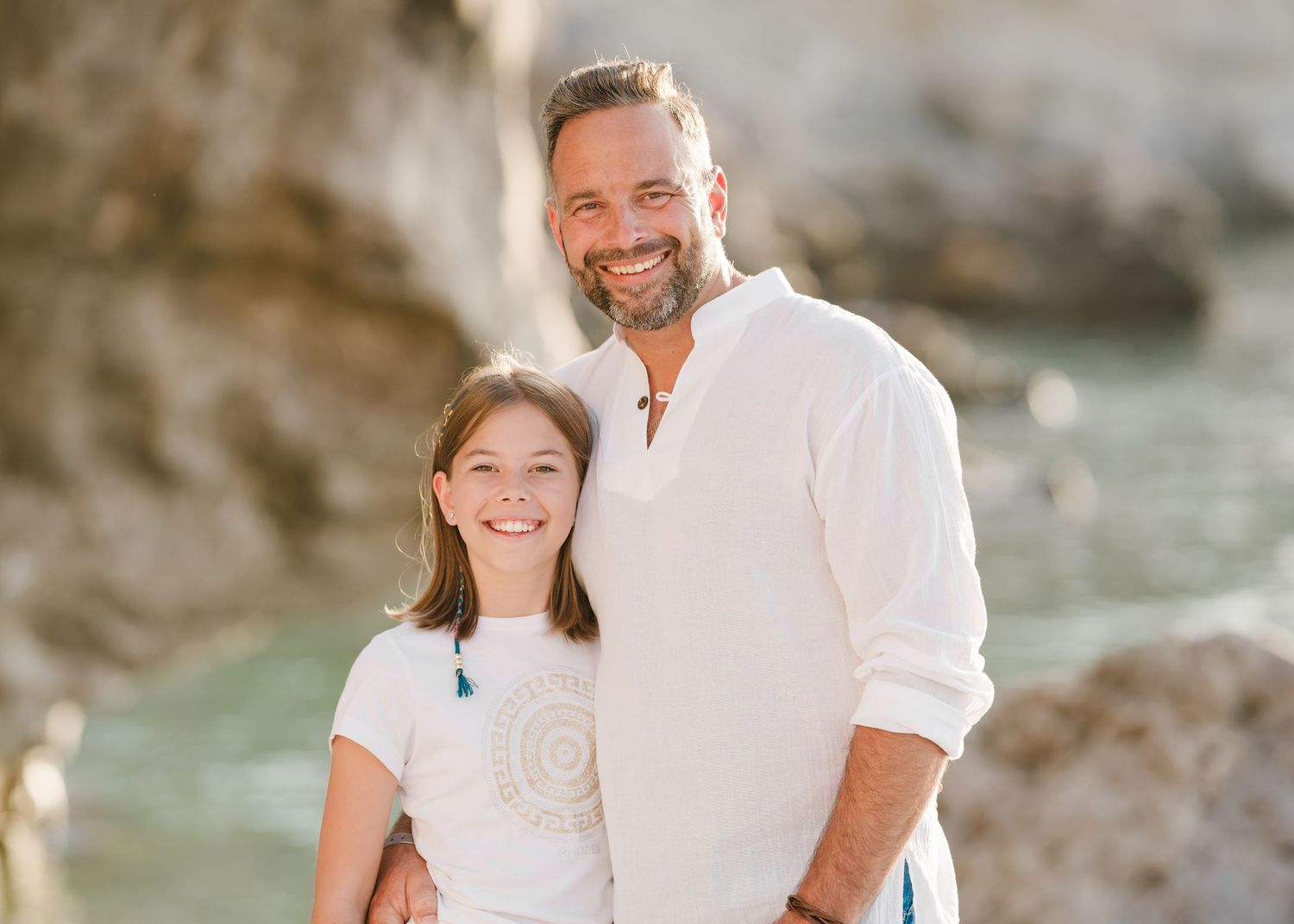 A warm portrait of two people smiling against a backdrop of coastal cliffs and turquoise waters. Fotograf Rhodos