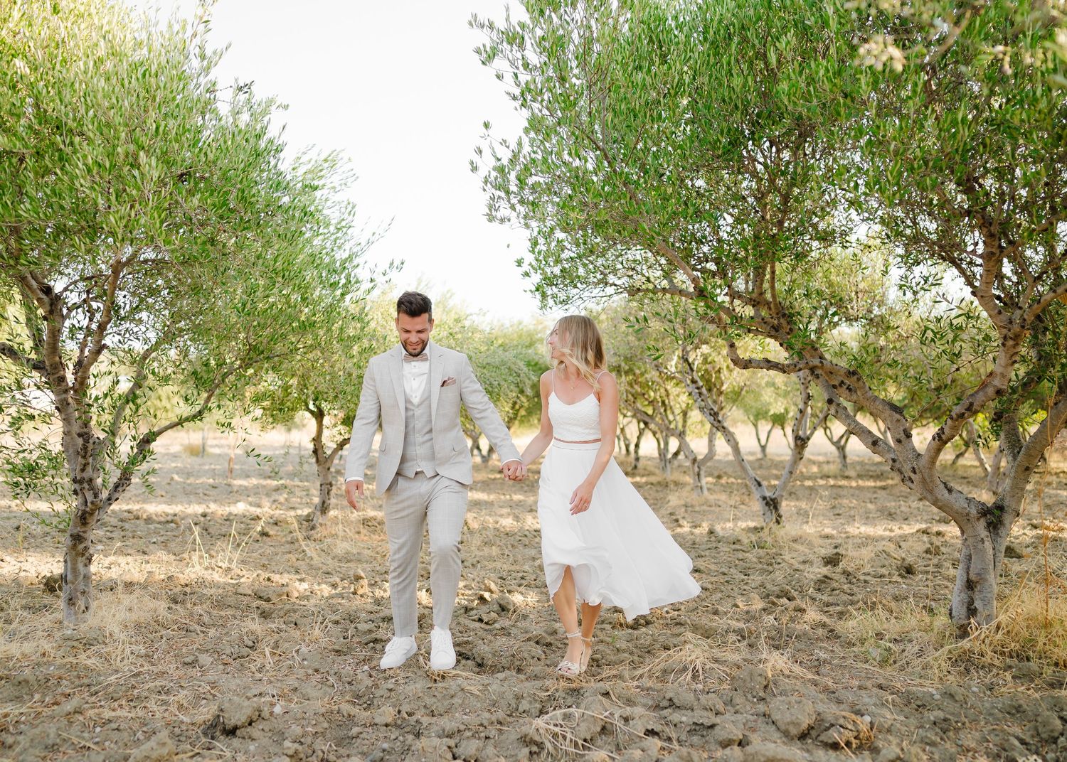 Ein romantisches Paar schlendert während eines Fotoshootings zum goldenen Sonnenuntergang Hand in Hand durch einen Olivenhain.