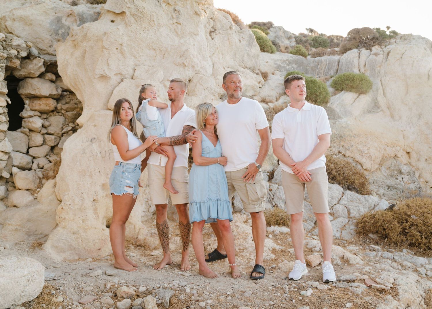 Family group wearing coordinated white and blue outfits posed against rocky cliff background. Fotograf Rhodos
