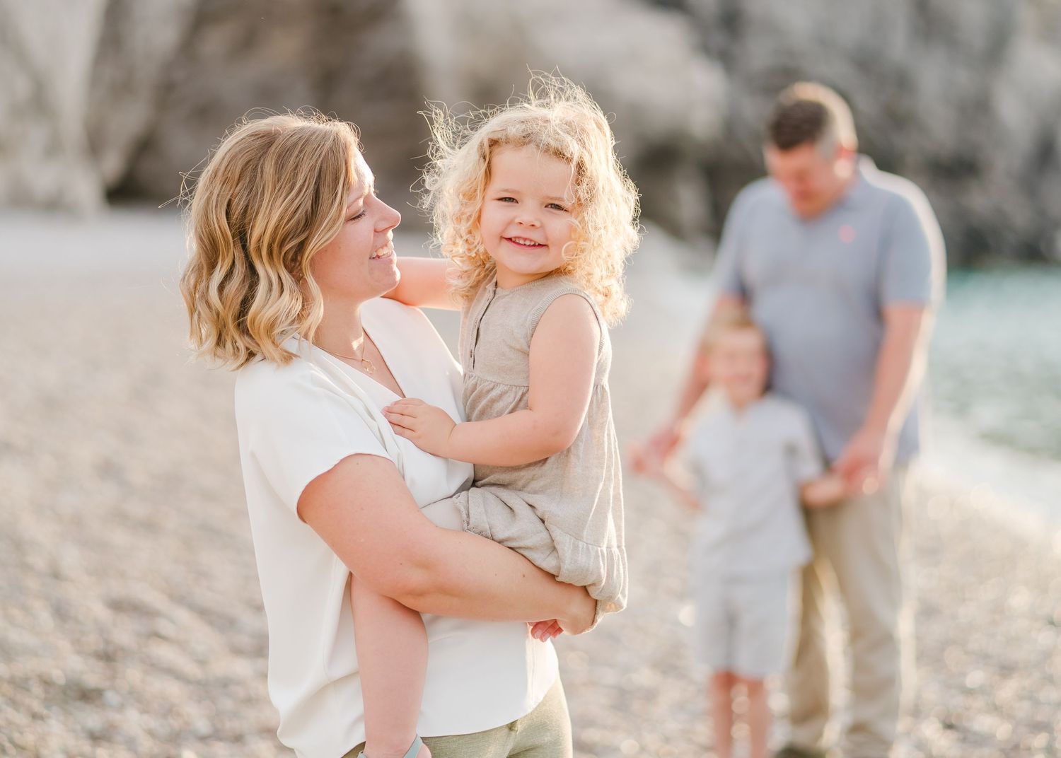 Family enjoying tender moments together on pebble beach near rocky cliffs. Fotograf Rhodos