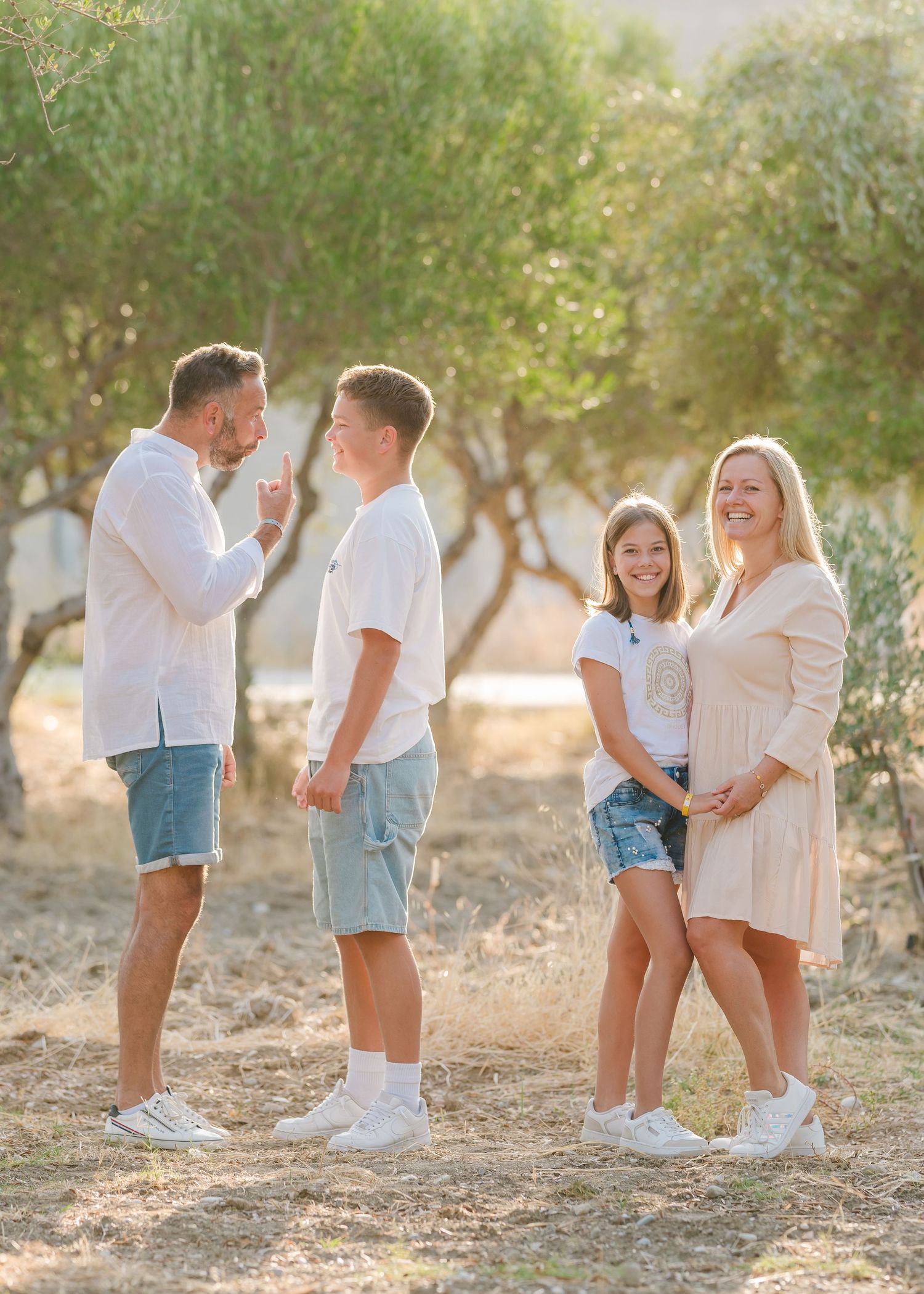 Family playing together in a sun-drenched olive grove wearing coordinated white and blue outfits. Fotograf Rhodos