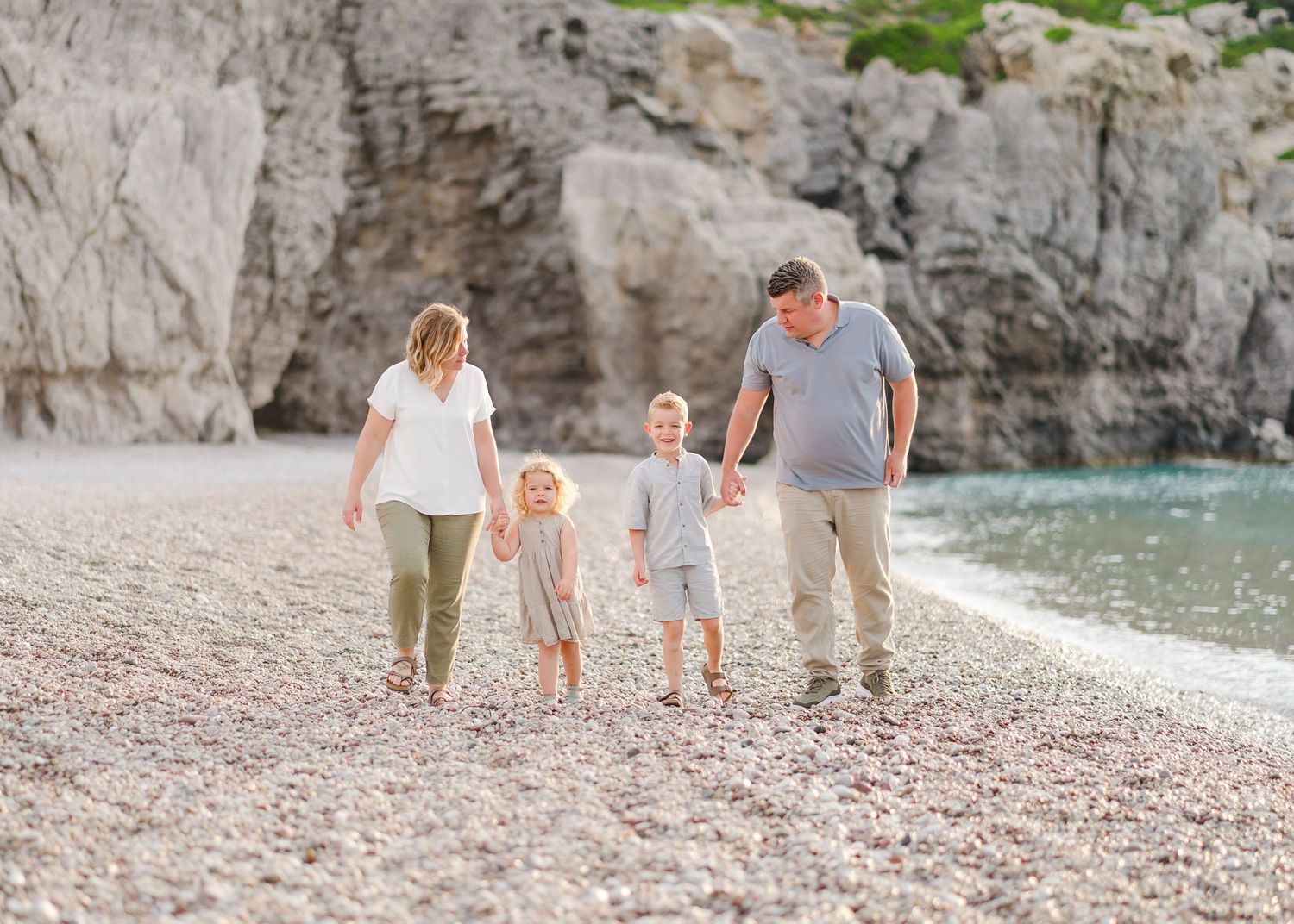 A family walks together along a rocky beach with cliffs in the background. Fotograf Rhodos