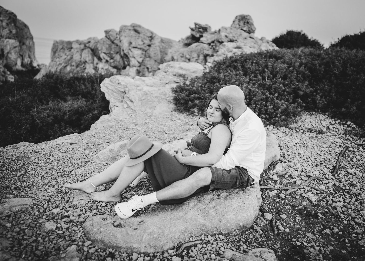 A black and white photo of two people relaxing on rocky coastal terrain.