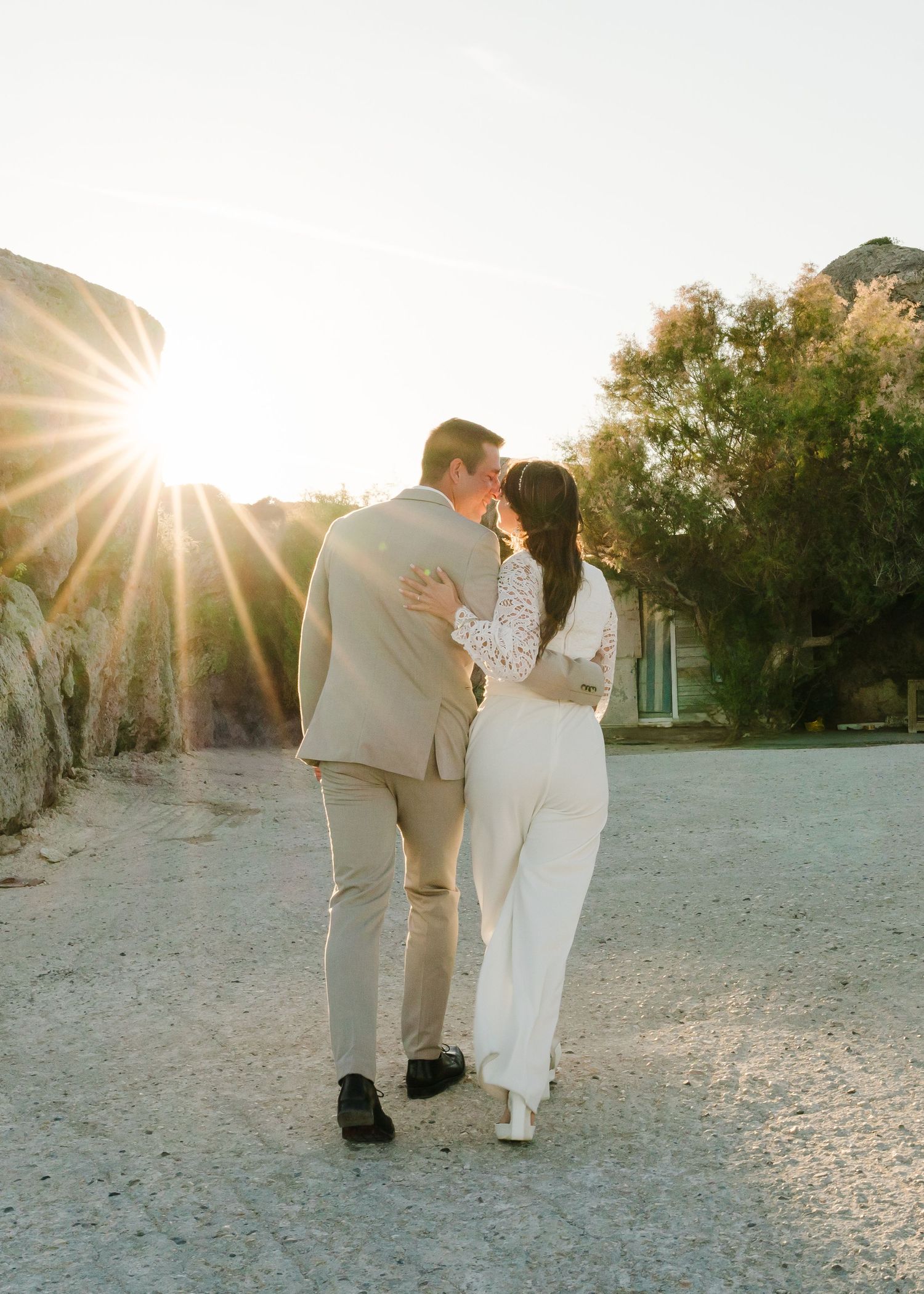 Frischvermählte gehen Hand in Hand vor einer felsigen Wüstenkulisse mit goldenem Sonnenlicht. Strandhochzeit Rhodos - Hochzeitsfotograf Rhod